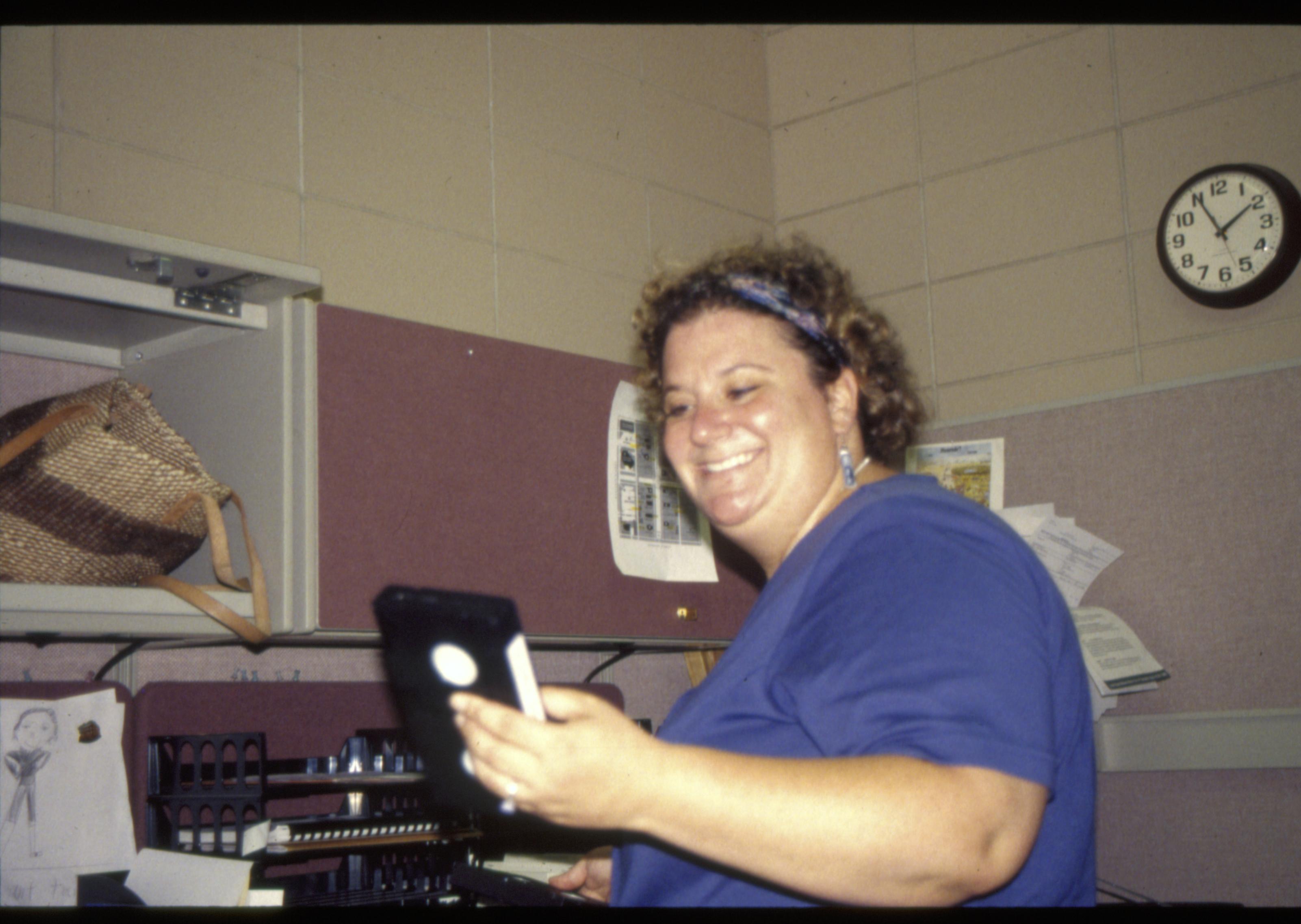 Museum Intern Terry Fingerhut holding a VHS tape at her desk in the Lincoln Barn. Looking Southeast in the main office room (former Men's room) staff, Museum, Lincoln Barn