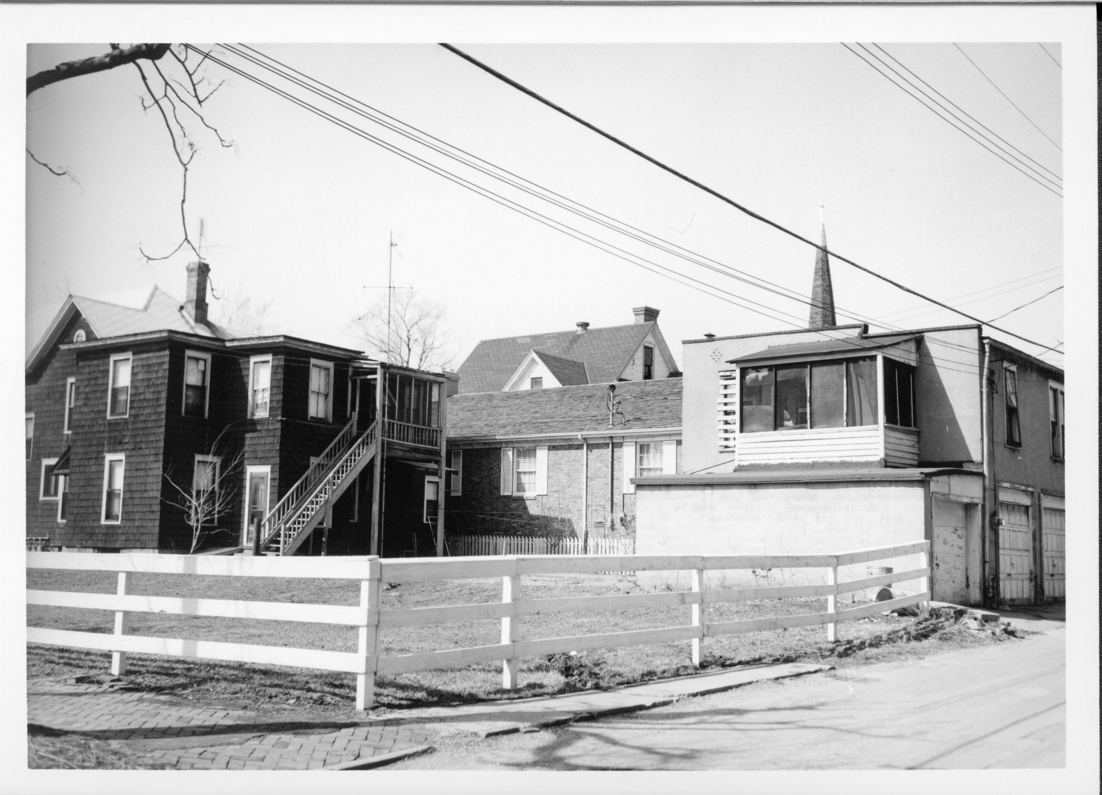 Dark shingled house and two-story garage on right belonging to Eleanor J. Pruett on Block 7, Lot 7 along 7th Street.  Brick building in center was used by Springfield Marine Bank.  Gabled house in background belonged to Eugene McNally. Located where Visitor Center is now. Looking Northwest from alley Pruett, McNally, Springfield Marine Bank, Visitor Center