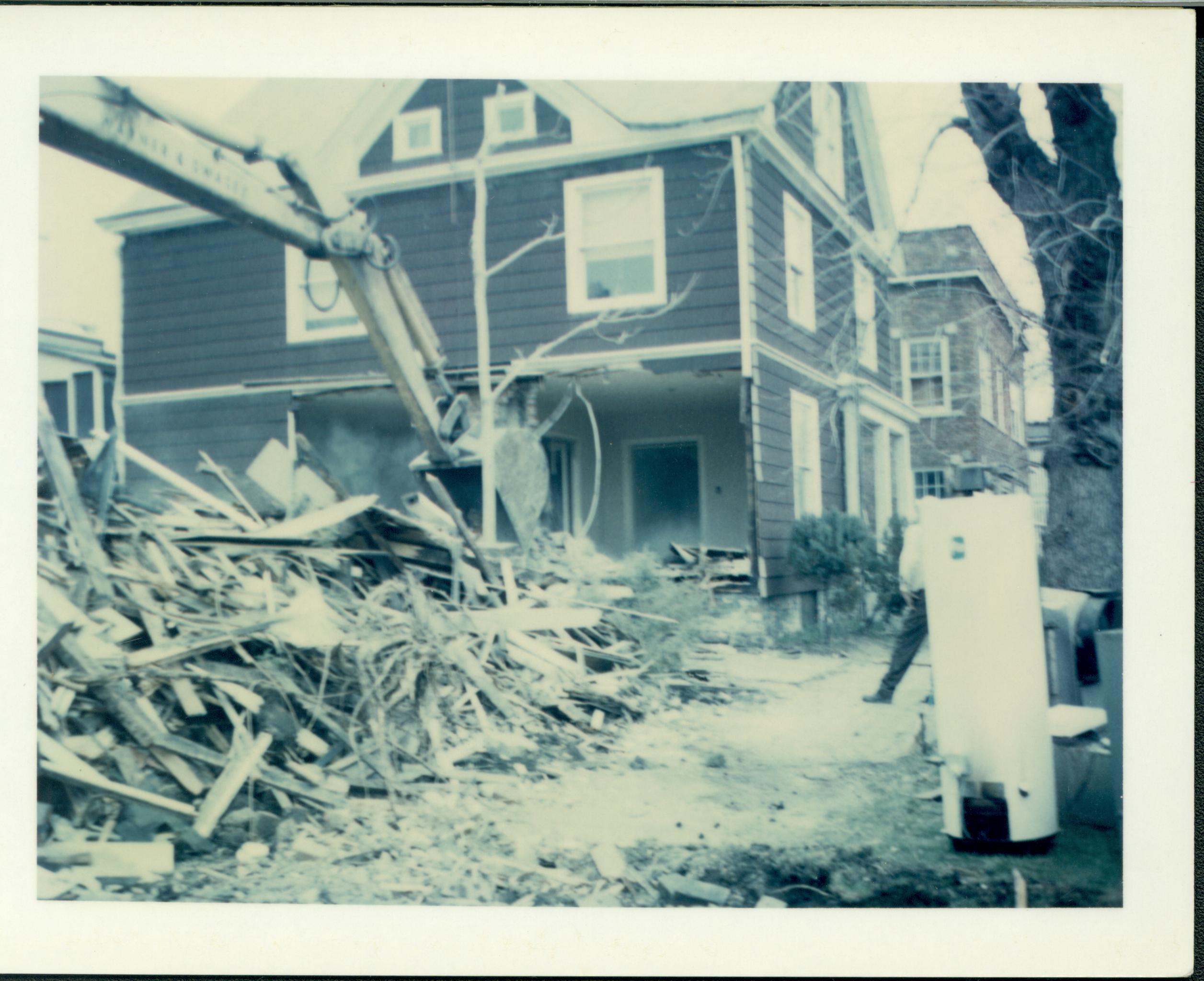 Duplex owned by William Sheeham in process of being razed, Block 7, Lot 8 along Jackson Street. Clapboard house in background owned by William Hermes.  Brick building in background right owned by Herman Hofferkamp. Area is now Visitor Center.  Old water heater on curb on far right. Looking East/Northeast from 7th and Jackson Street. Sheeham, Hermes, Hofferkamp, Jackson Street, Visitor Center, razing