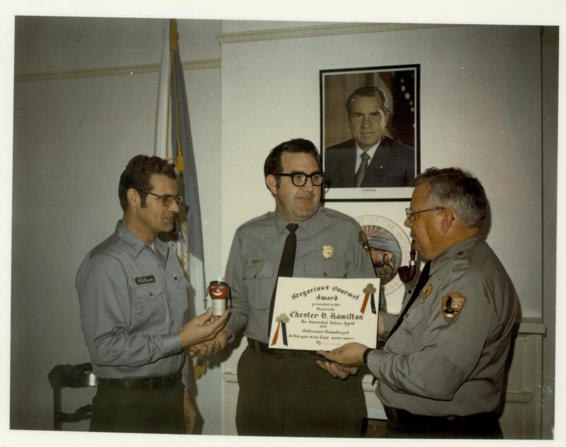 Special award to Ranger Chet Hamilton given by Maint. staff Bob LaFrance and Supt. Al Banton for trip to and from Mid-West Regional office.  Given in Supt. office in Lyon House looking West awards, staff, Lyon, humor