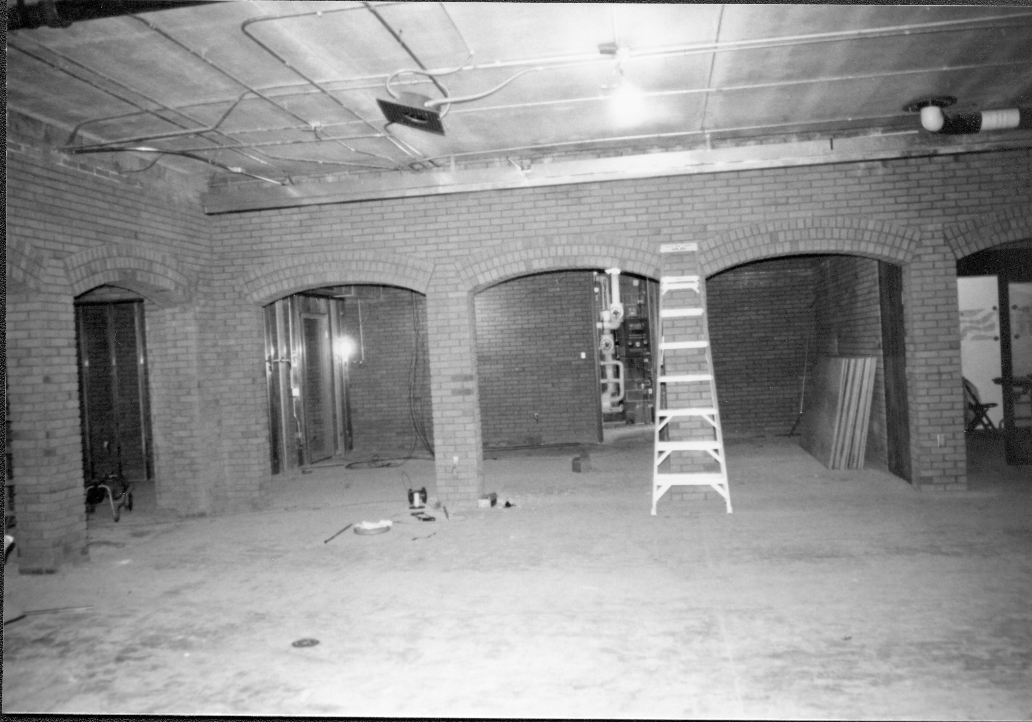 Visitor Center - remodeling, main area with bookstore area in background. Restroom arches on left.  Bookstore storage area visible on center left. Open door to boiler room in background center behind ladder. Office area visible through open door on right. Looking East from main area Visitor Center, remodeling, bookstore, boiler room, office, main, restroom, storage