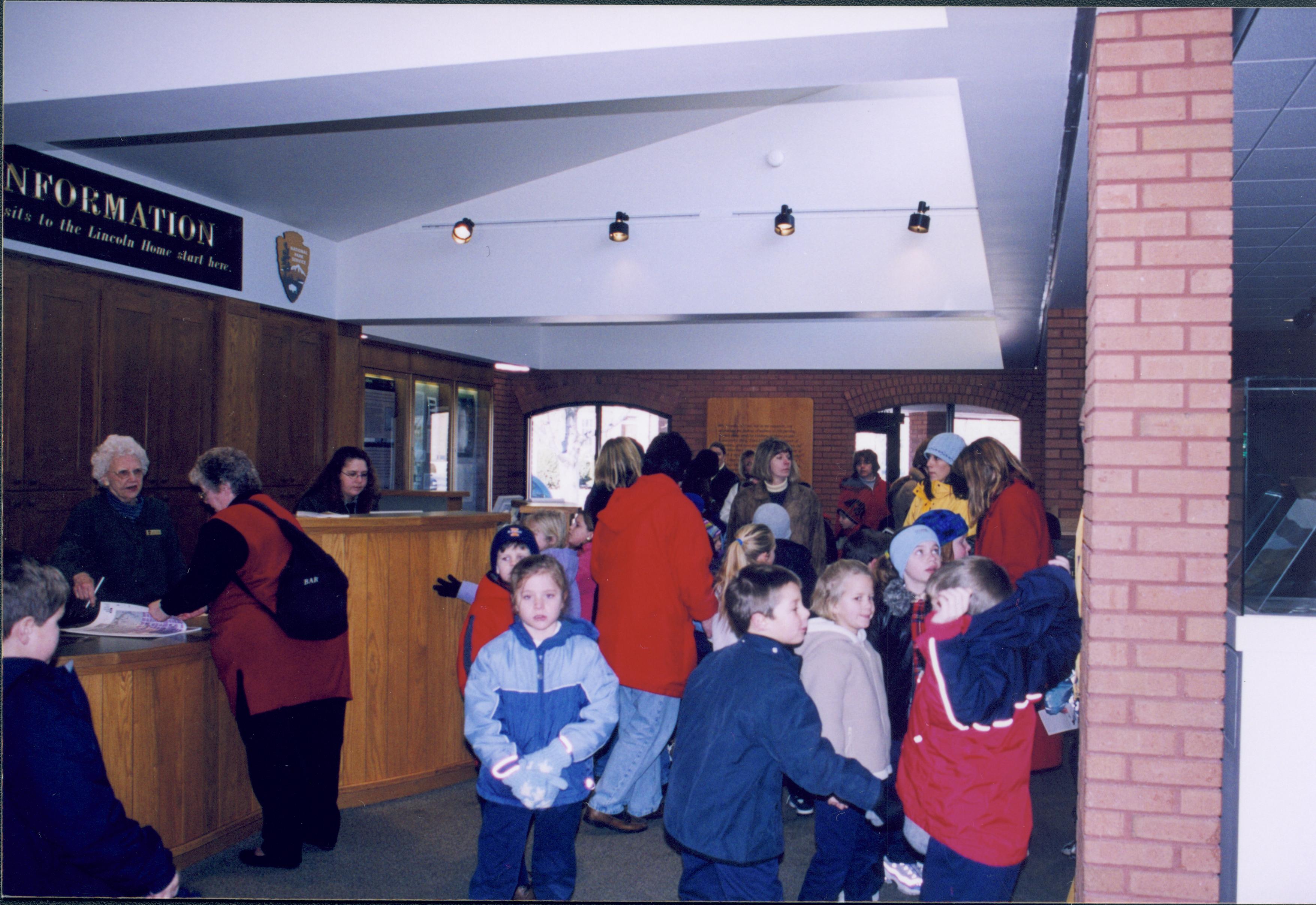 Lincoln's Birthday - School group visiting site during activities. Volunteer ? assists lady in red coat. Ranger Christy Lindberg works behind the desk.   Looking Northwest from main area Lincoln's Birthday, Visitor Center, school group, staff, volunteers, visitors