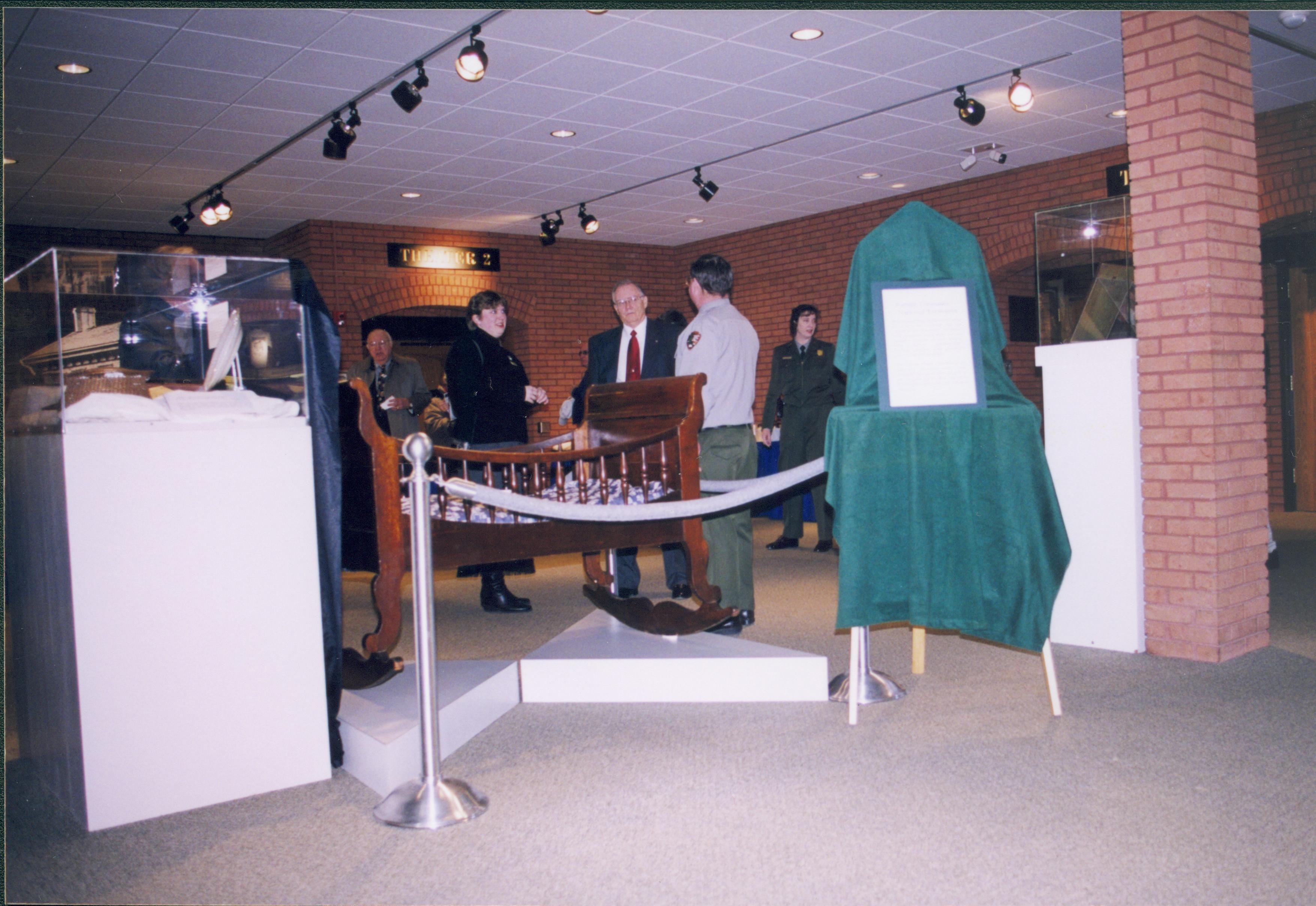 Lincoln's Birthday - Cool Lincoln Stuff exhibit set up in main Visitor Center area.  The Lincolns' cradle is in center. Visitors mill around.  Curator Susan Haake and Ranger Jim Ranslow talk to Acting Superintendent Jim LaRock.  Ranger Cat Mancuso is in the background right.  Looking Southeast from information desk area. Lincoln's Birthday, exhibit, staff, visitors, Visitor Center