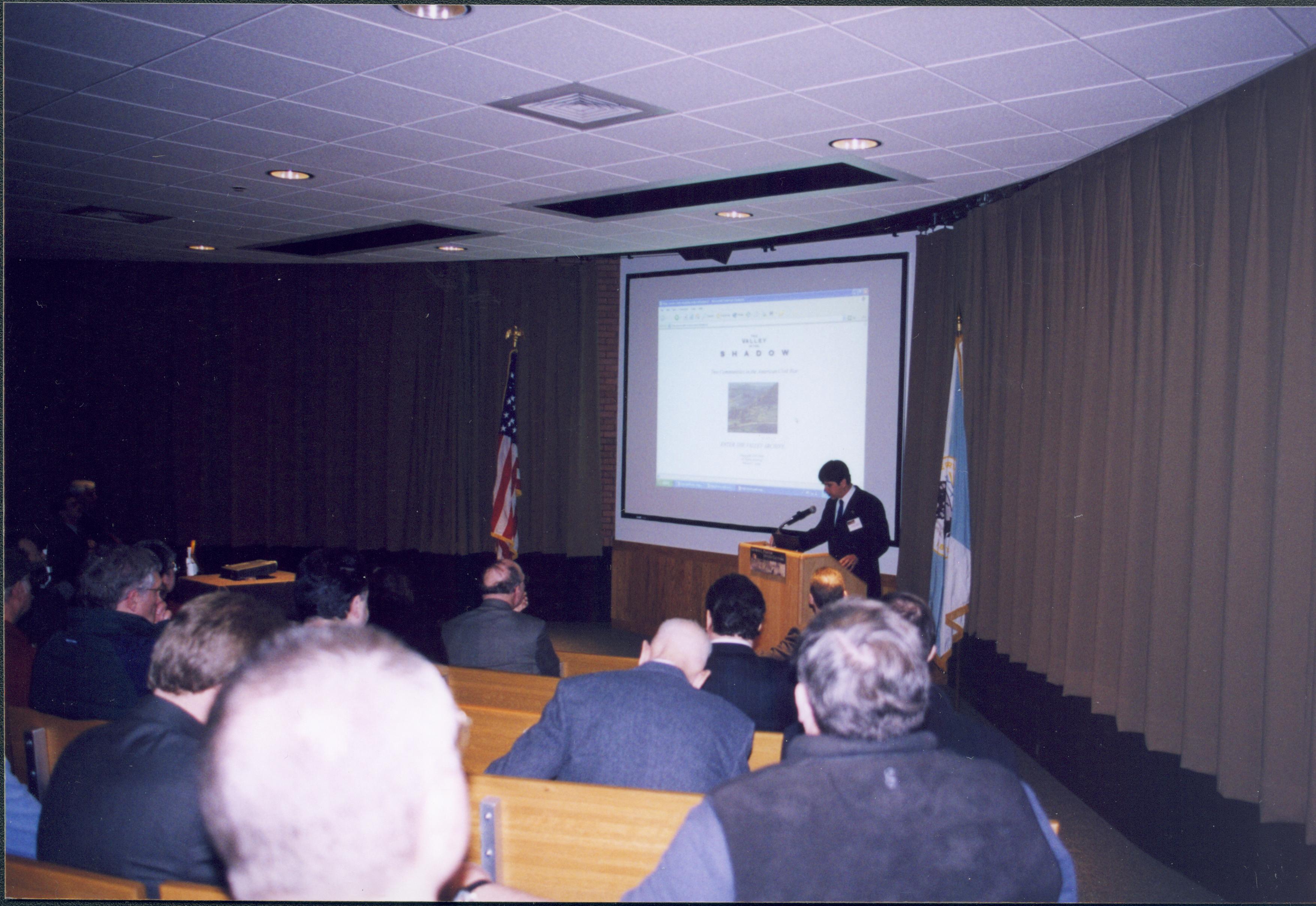 Lincoln's Birthday - Speaker William G. Thomas delivers a lecture and powerpoint program to crowd in Visitor Center. Curtains pulled back partly to allow for screen. Flags flank screen area and podium in front of theater Looking Southwest from back of Theater 1 Lincoln's Birthday, lecture, Theater 1, Visitor Center, visitors, flags, podium, screen