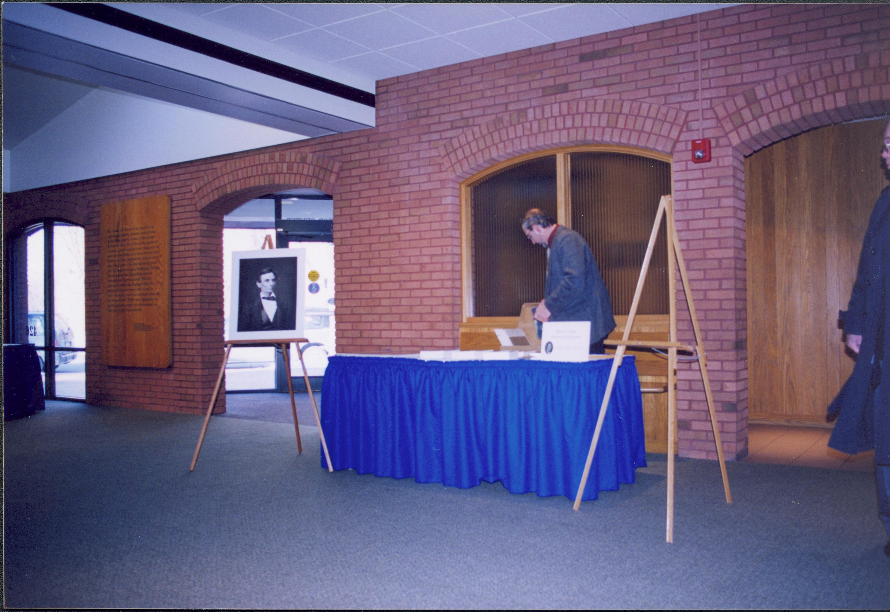 Lincoln's Birthday - Illinois State Historical Society Director Bill Furry setting up information table in Visitor Center lobby. A visitor watches from far right. Restroom arch on right, 7th Street entrance on left near Farewell Address exhibit. Looking Northwest from main area Lincoln's birthday, exhibit, Illinois State Historical Society, visitors, Visitor Center