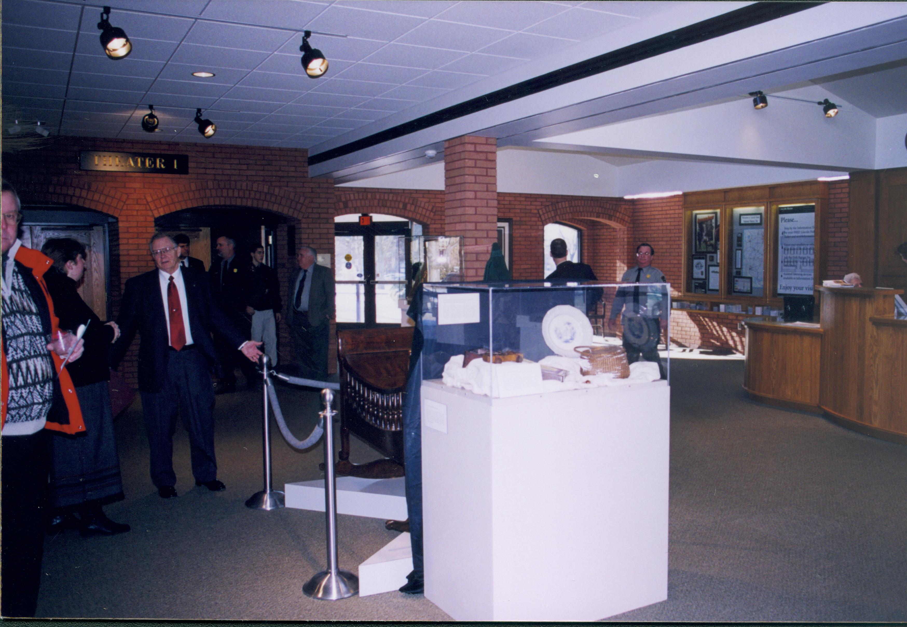 Lincoln's Birthday - Cool Lincoln Stuff exhibit in foreground including Mary Lincoln's sewing basket and a pull toy made by Lincoln. Curator Susan Haake talks to Acting Superintendent Jim LaRock; former Superintendent Dick Lusardi in background near Theater 1 doors. Historian Tim Townsend (back to camera) talks to Ranger Jim Ranslow behind exhibit. Ranger Cat Mancuso on far right. Looiing Southwest from main area Lincoln's birthday, exhibit, lecture, staff, Visitor Center, visitors