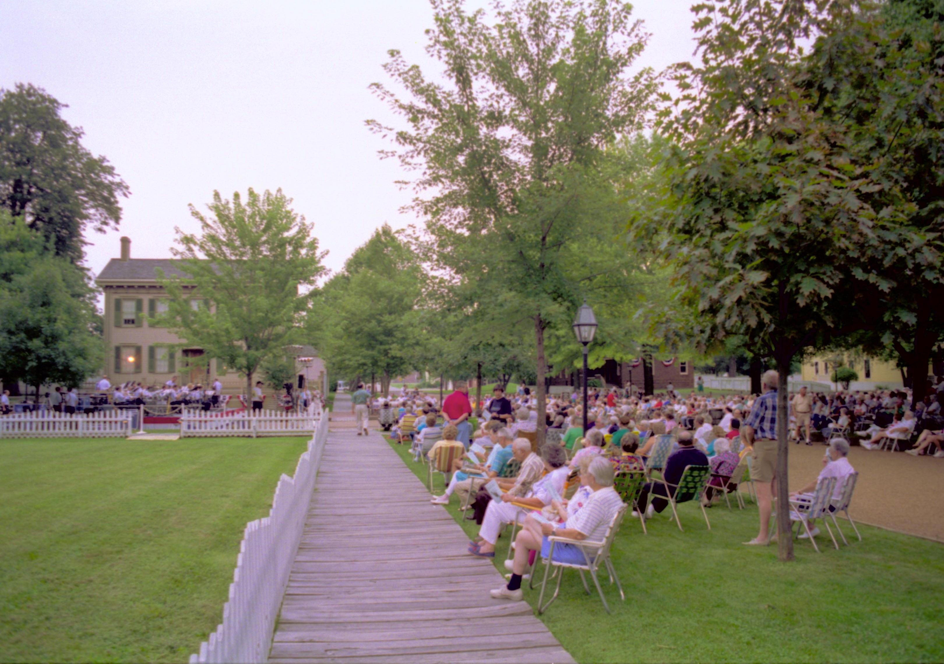 People seated listening to Coast Guard band with Lincoln home in background. Lincoln Home NHS- Coast Guard Band Concert, 267618 concert, Coast Guard