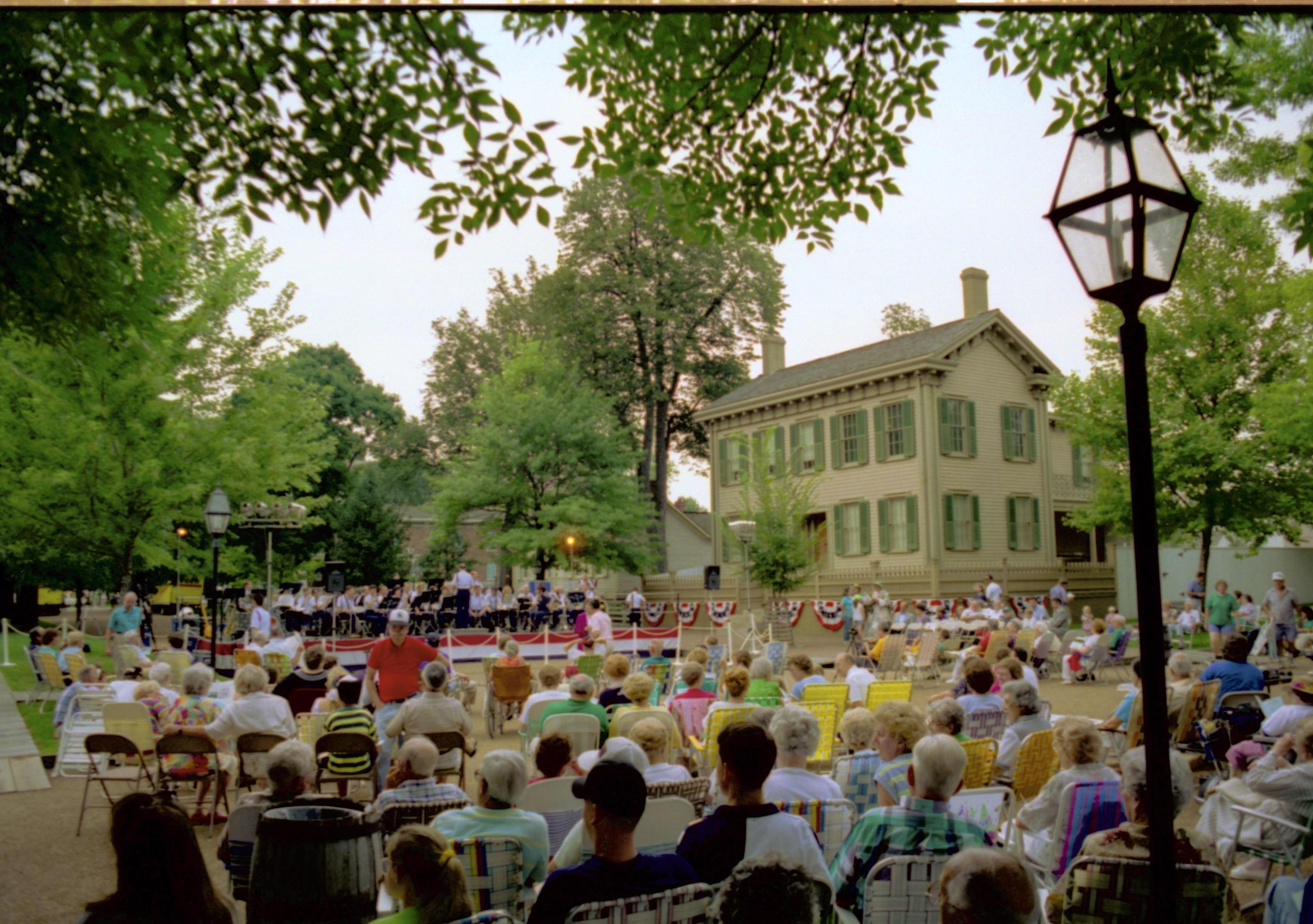 Public seated, band on platform and Lincoln home in background. Lincoln Home NHS- Coast Guard Band Concert, 267618 concert, Coast Guard