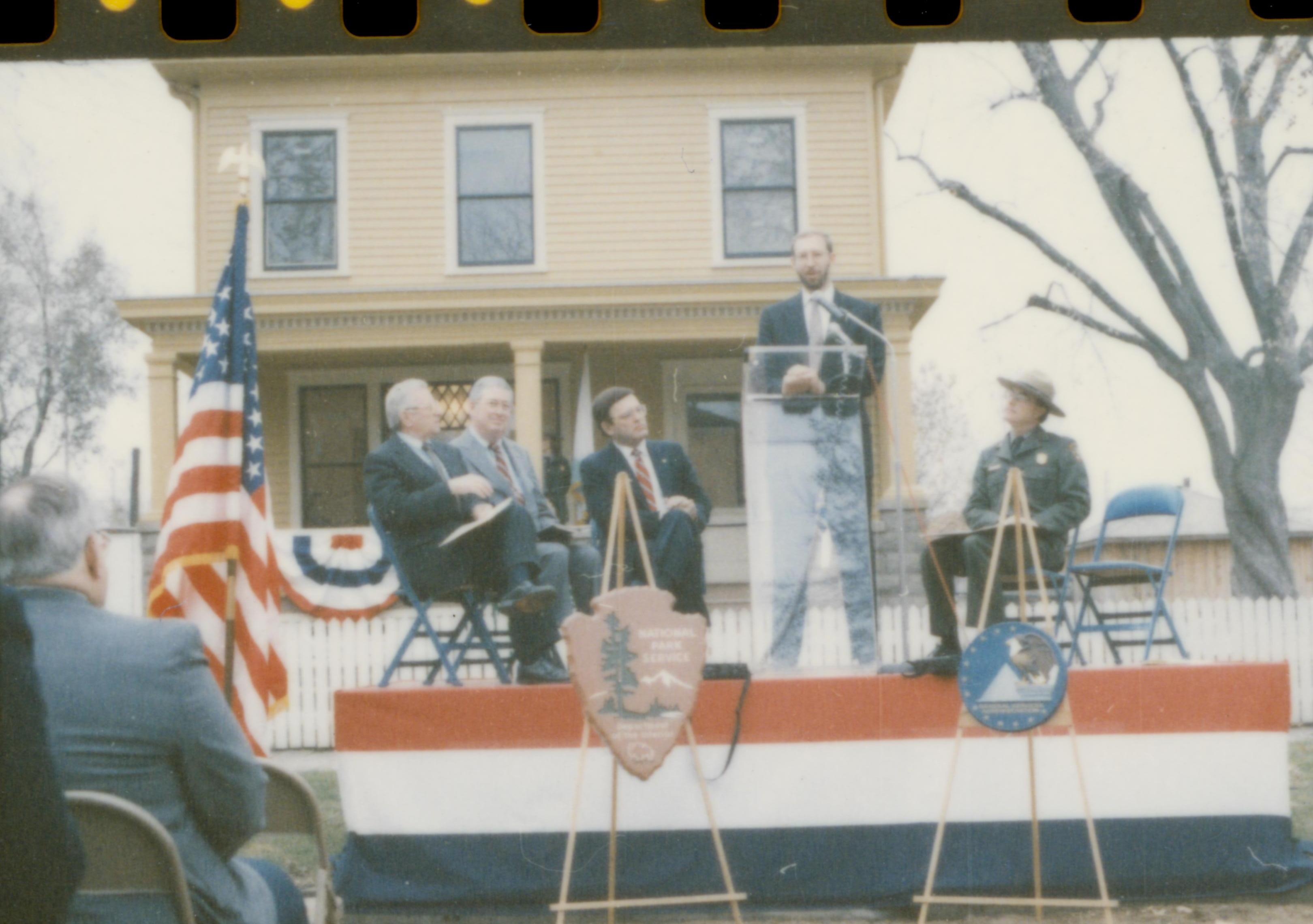 Five men on speakers platform in front of Cook house Lincoln Home NHS- Cook House Re-opening, 1 Cook, ceremony