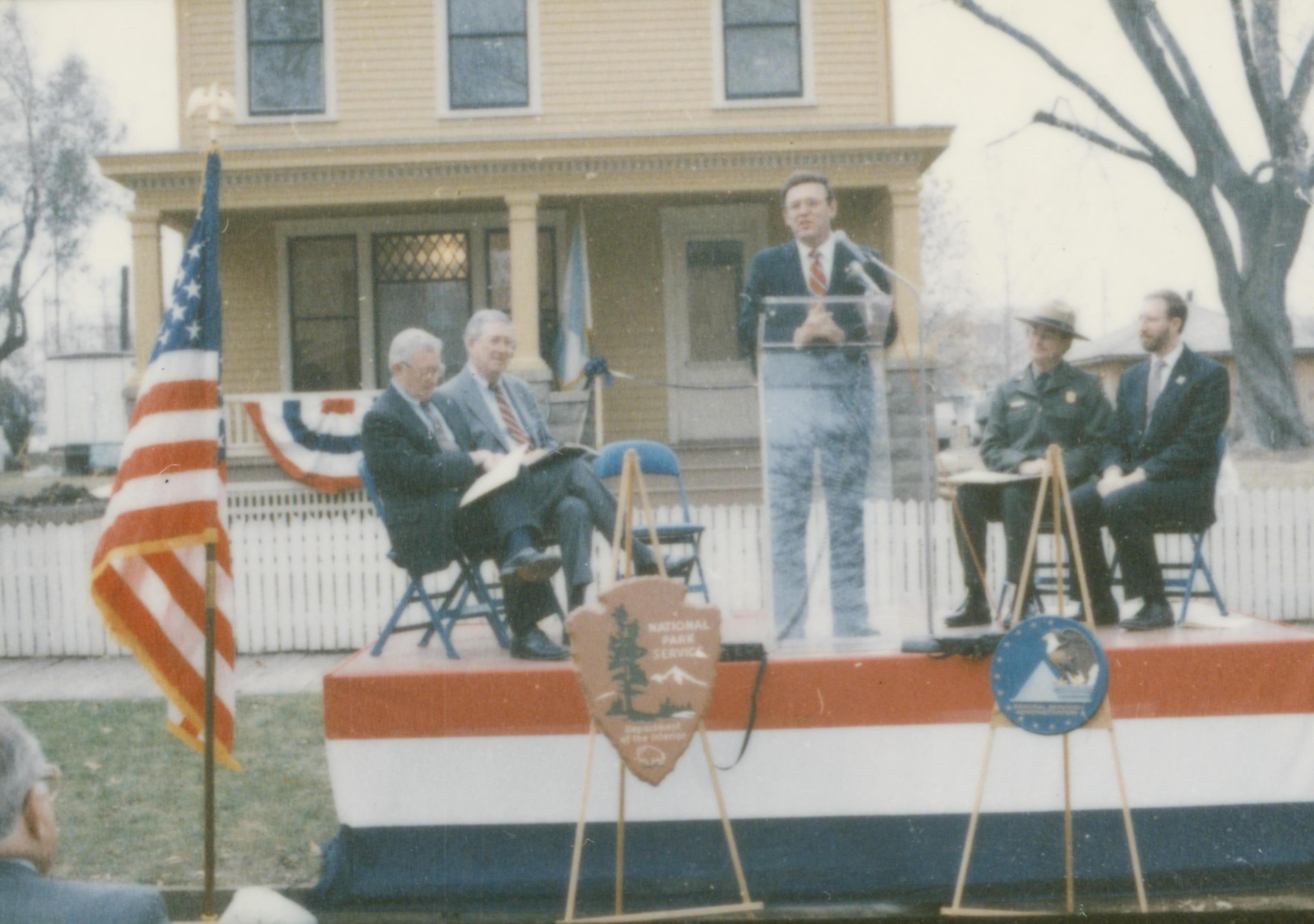 Five men on speakers platform in front of Cook house Lincoln Home NHS- Cook House Re-opening, 1 Cook, ceremony