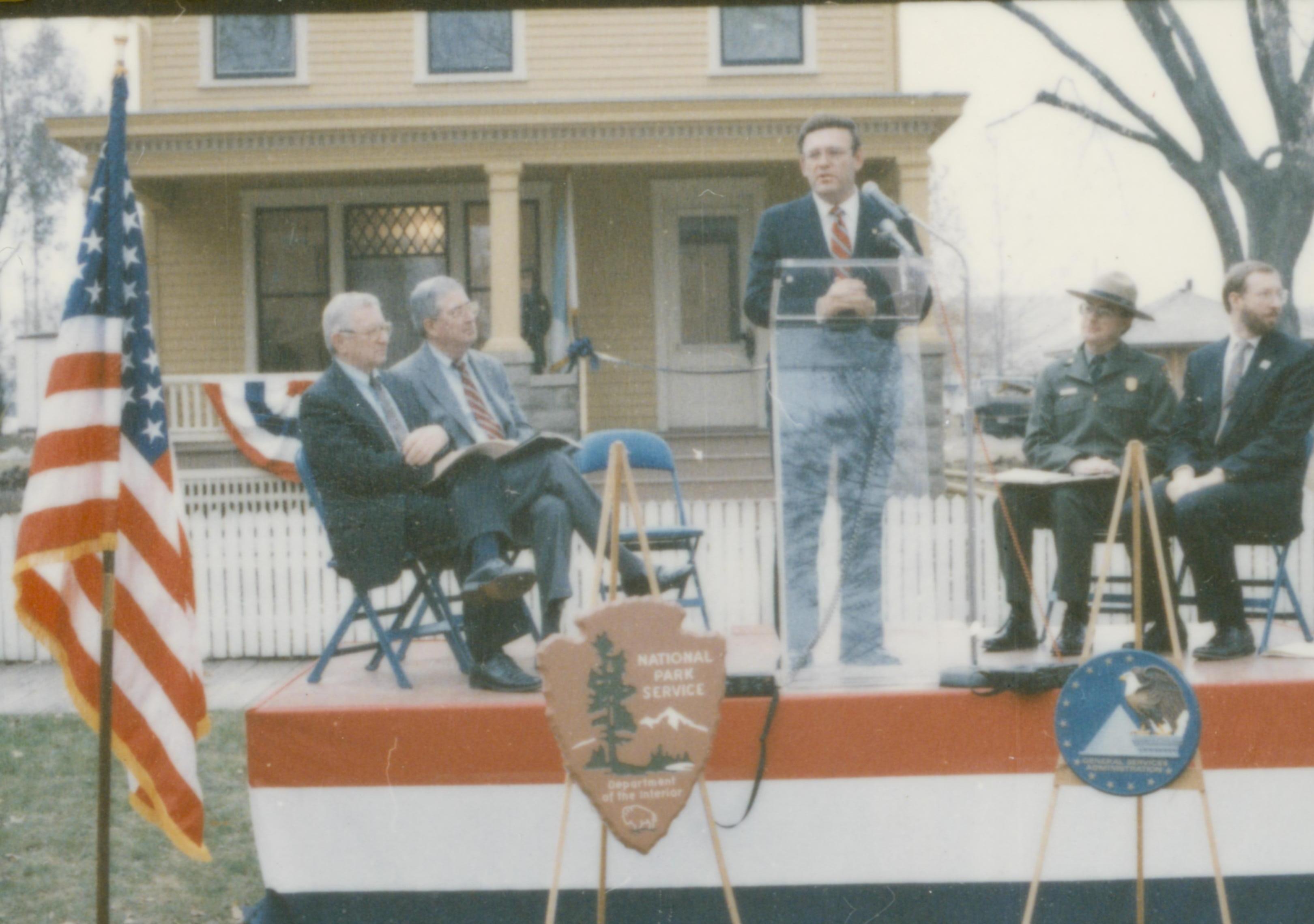 Five men on speakers platform in front of Cook house Lincoln Home NHS- Cook House Re-opening, 1 Cook, ceremony