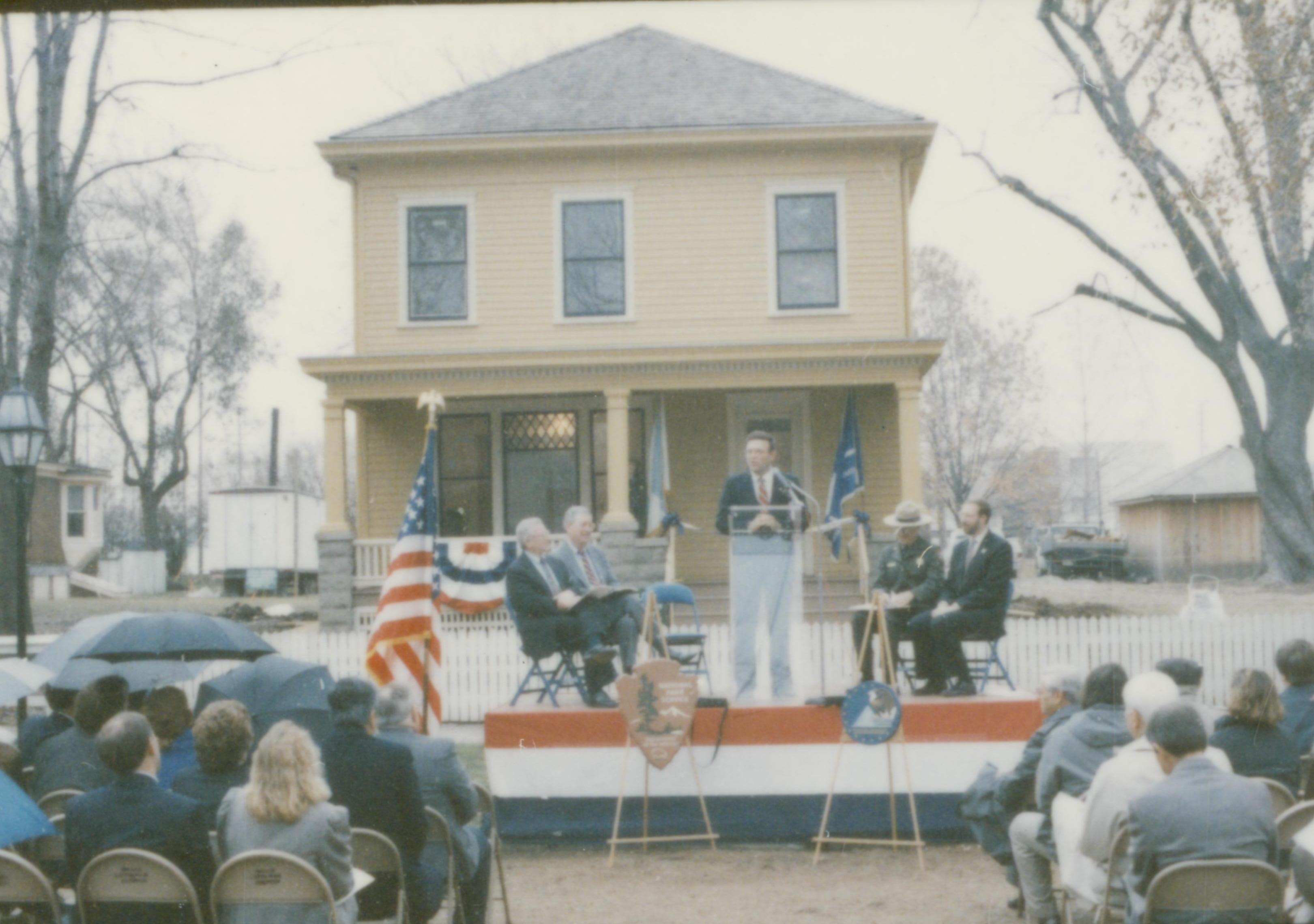 Five men on speakers platform in front of Cook house Lincoln Home NHS- Cook House Re-opening, 1 Cook, ceremony