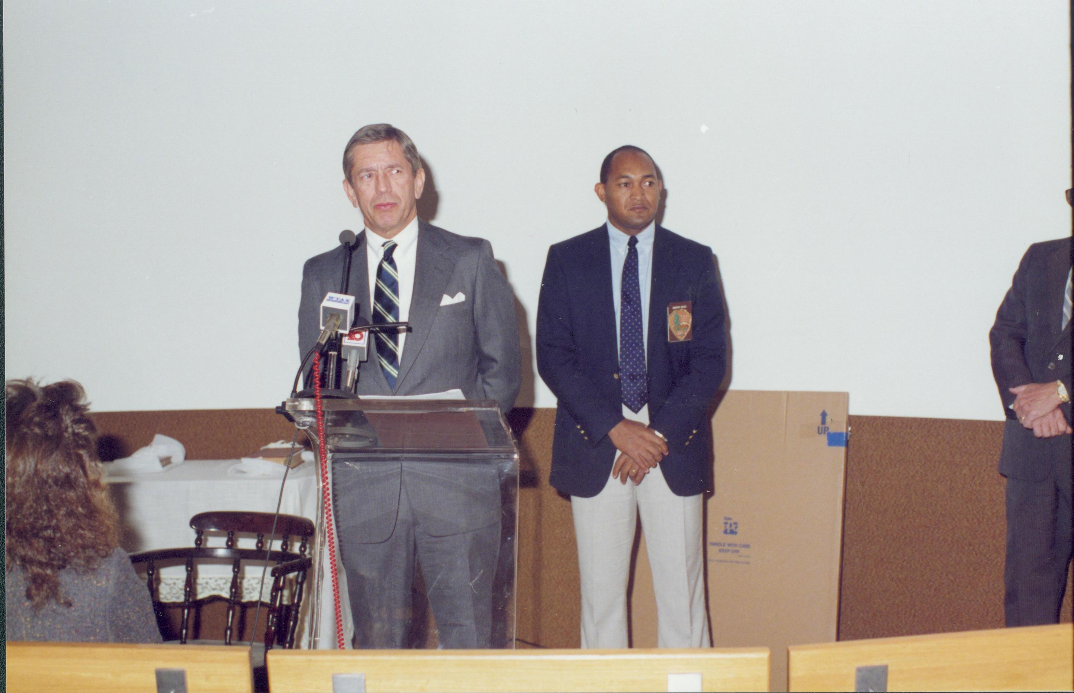 Two men (one speaking into microphone's) standing in front of screen. Lincoln Home NHS- Bring Furniture Back Home furniture, conference