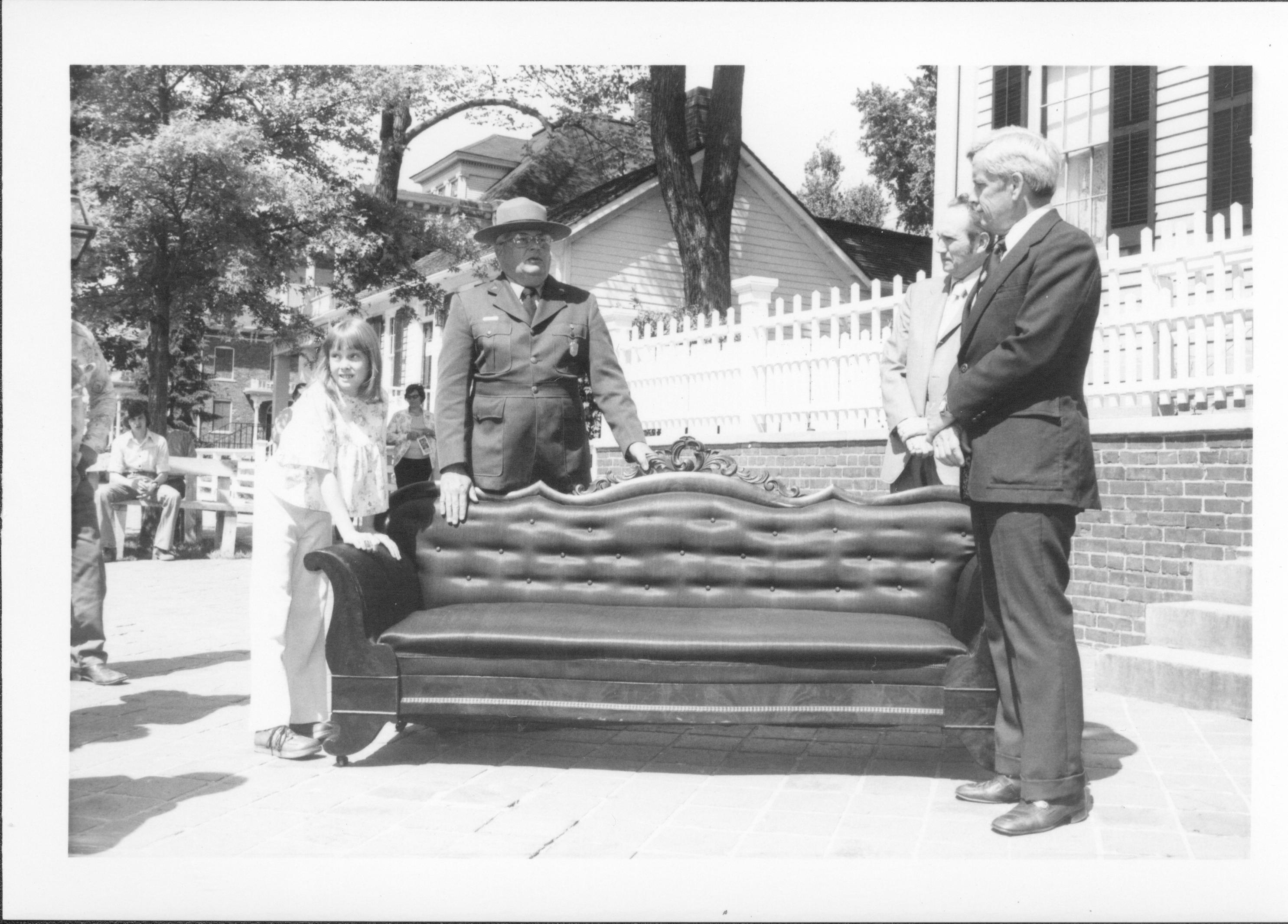 Three men and little girl standing around couch on siddwalk. Lincoln Home NHS- Bring Furniture Back Home, neg #14 class #1190, class 8 pic 14 furniture, return