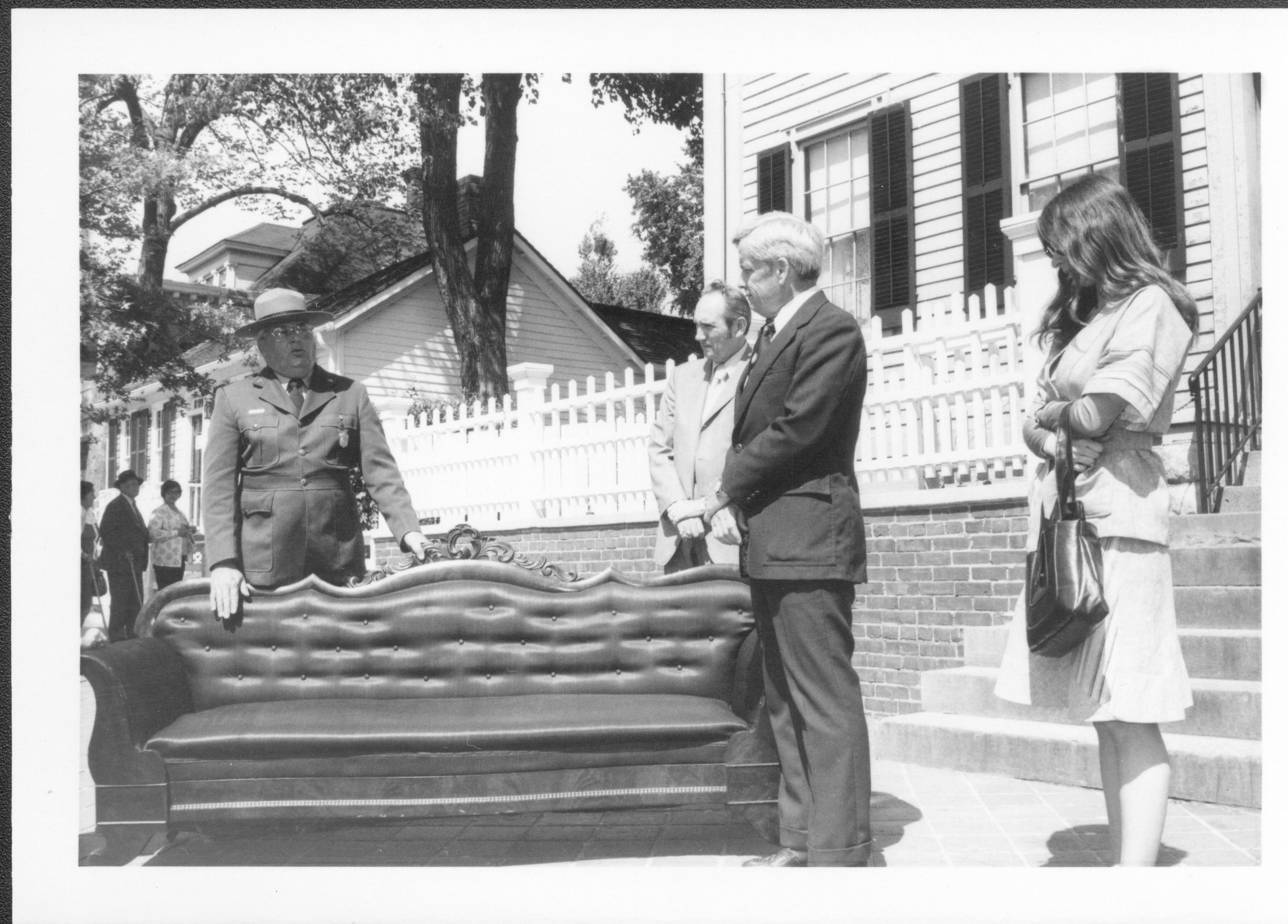 Three men and a lady standing around sofa on sidewalk. Lincoln Home NHS- Bring Furniture Back Home, neg #13 class #1190, class 8 pic 13 furniture, return