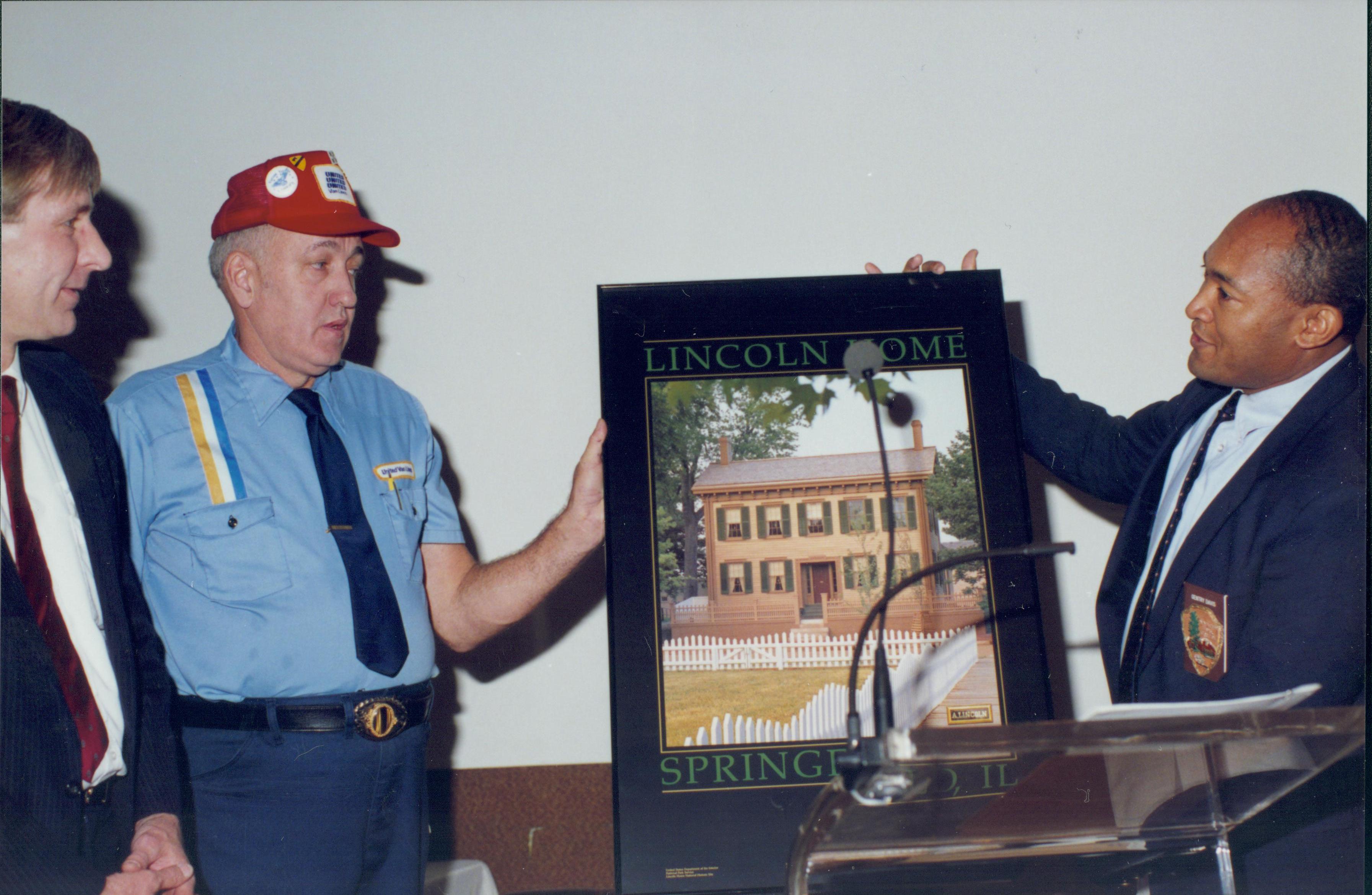 Two men holding Lincoln Home poster. Lincoln Home NHS- Bring Furniture Back Home presentation, picture