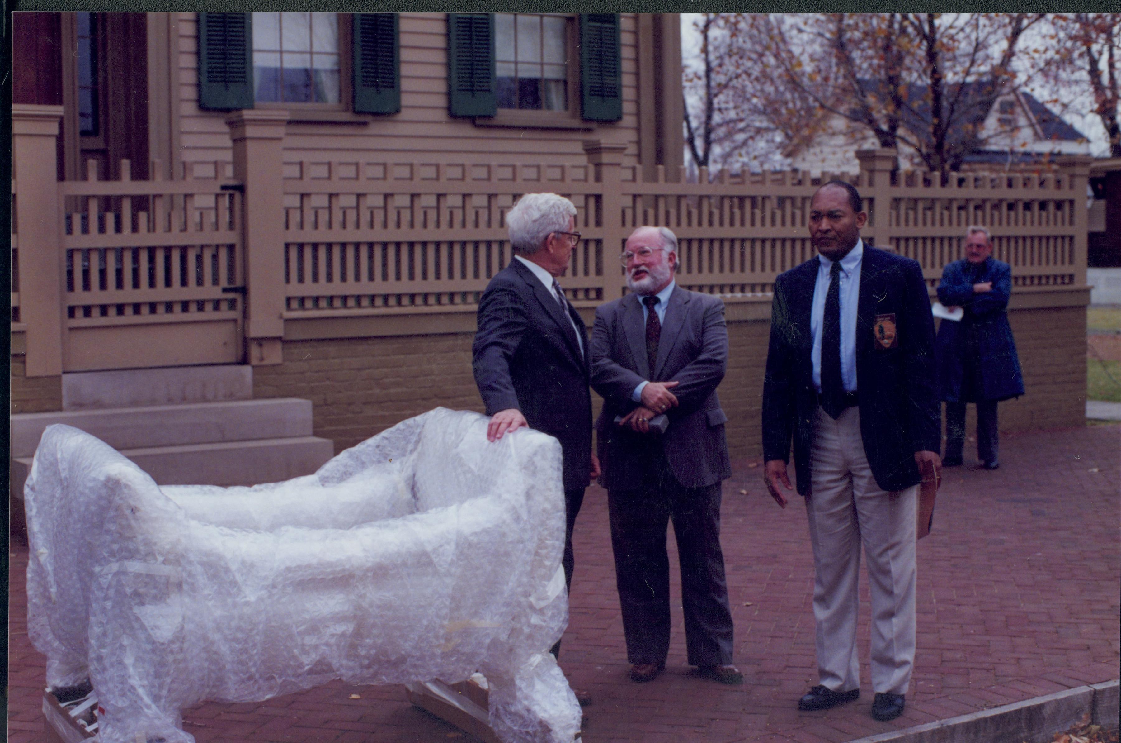 Three men standing with wrapped piece of furniture. Lincoln Home NHS- Bring Furniture Back Home furniture, movers