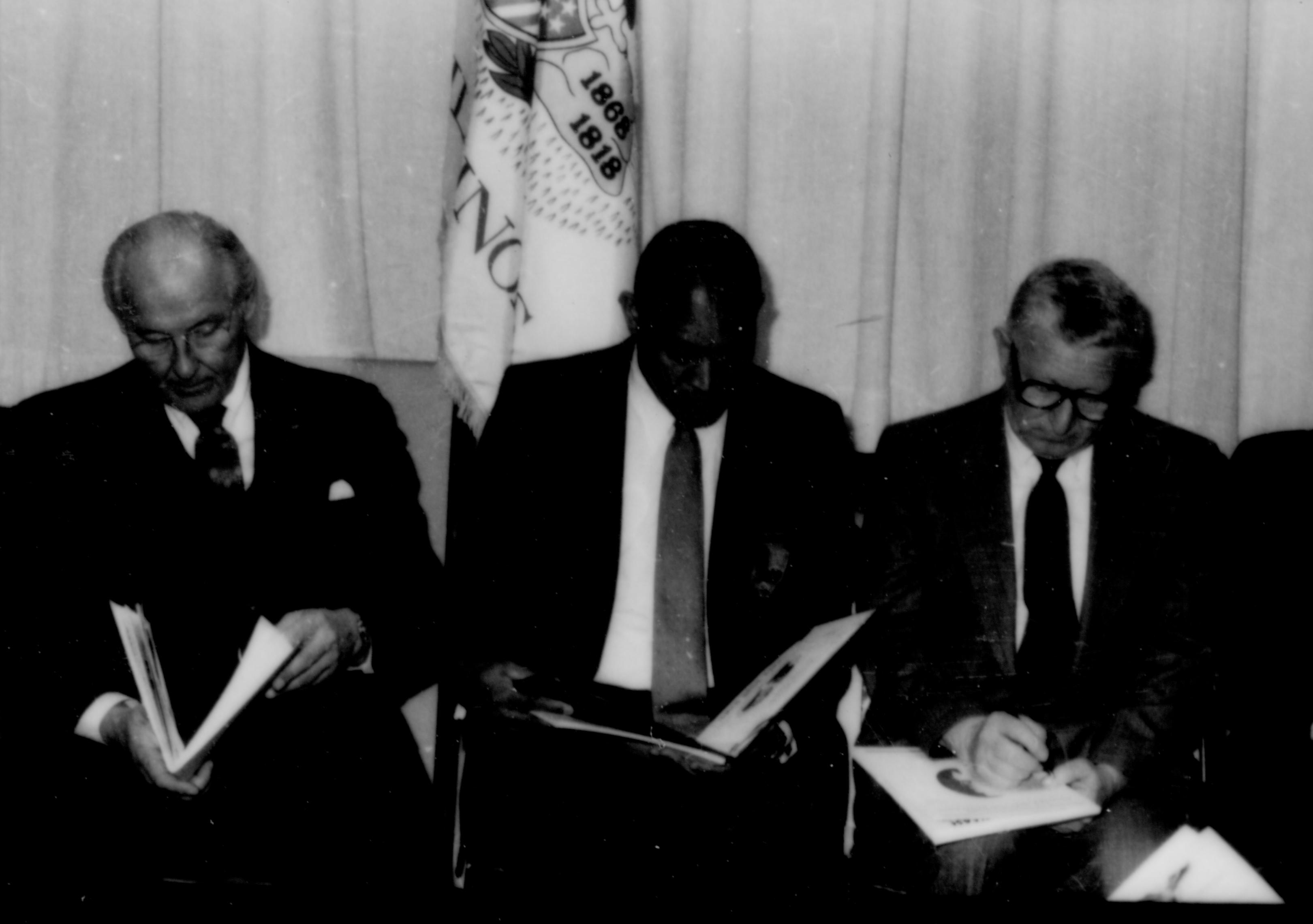 Three men seated looking at booklets. Lincoln Home NHS- Paul Findley and Michel VIP visit, 125 Finley, Michel, visit, program