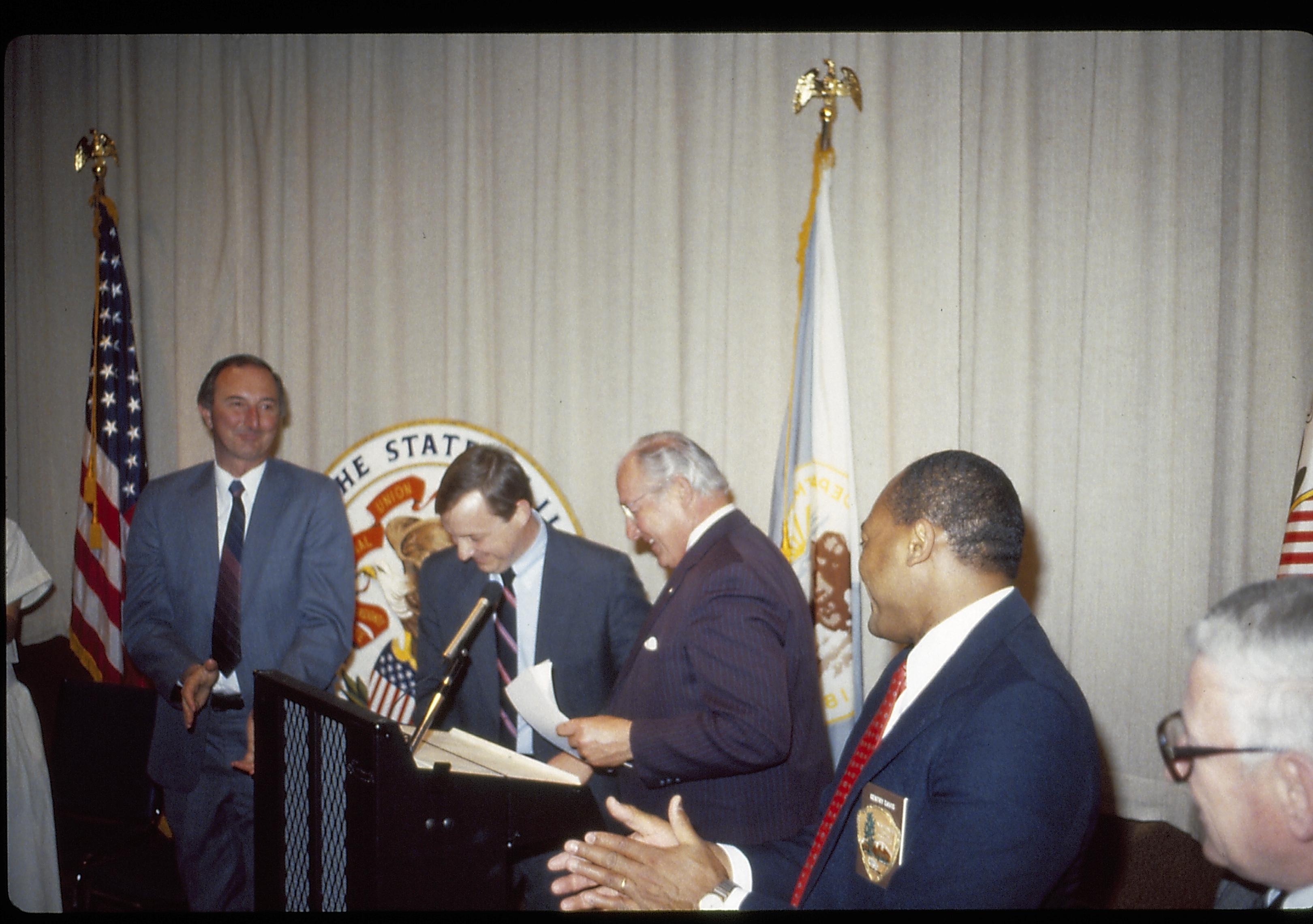 Group of men standing in VC theater in front of flasi, curtain and state seal. Lincoln Home NHS- VIP Findley and Michel Visit award, visit, ceremony