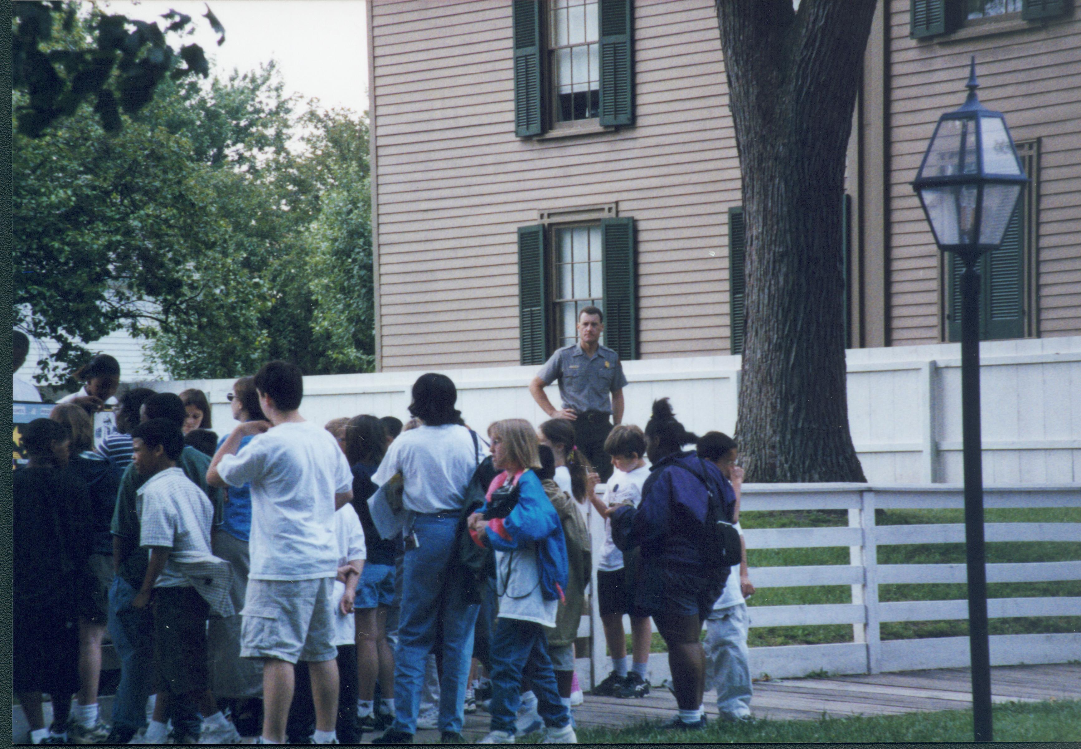 Iles School Living History program - Historian Tim Townsend surveys the crowd watching the Women's Rights performance in the Carrigan lot (Block 10, Lot 6-7).  Lincoln Home in background. Looking Southeast from 8th Street Iles School, living history, staff, students, school groups, Lincoln Home