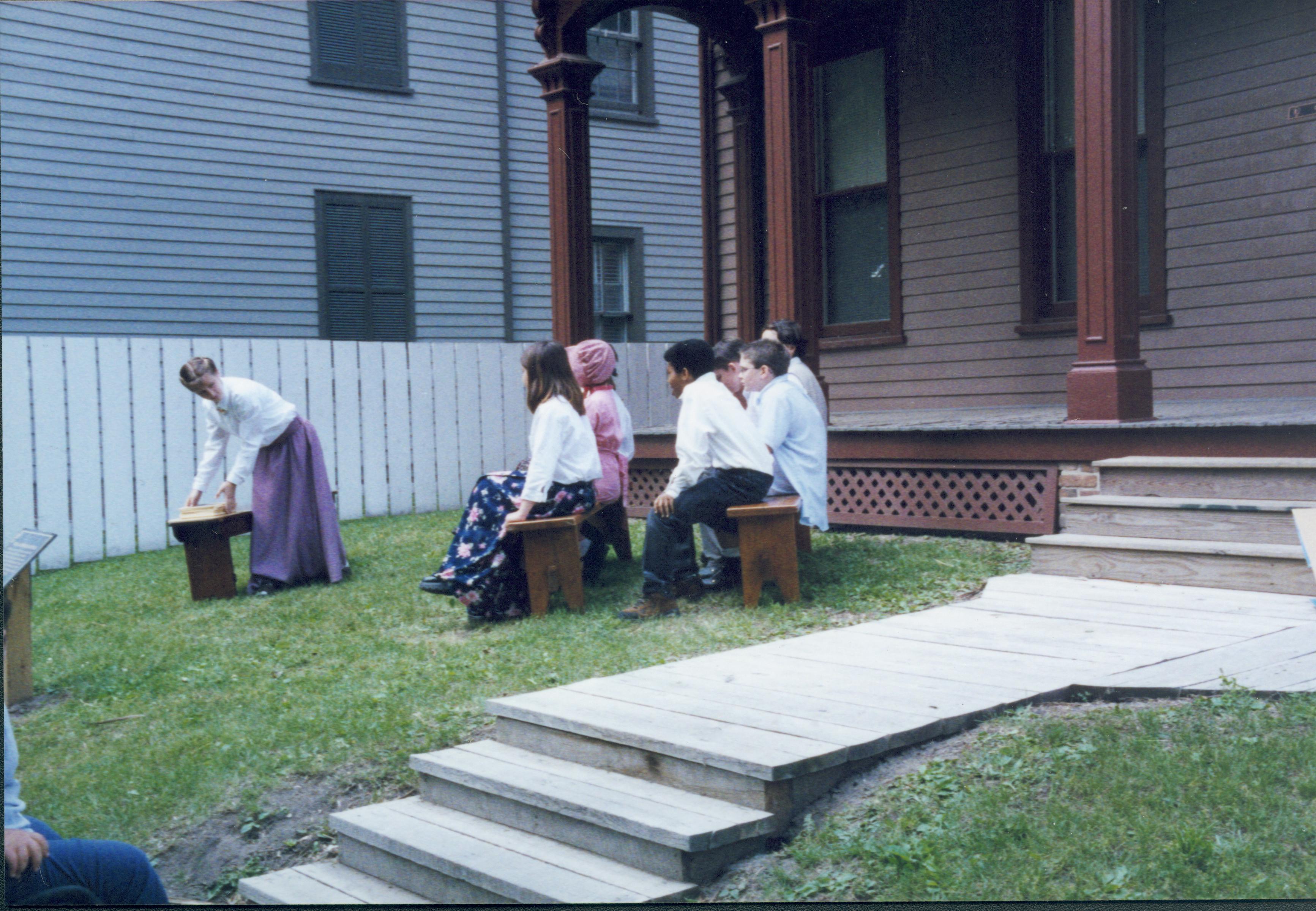 Iles School Living History program - Students performing skit on 19th century education on benches in Beedle House lawn. Visitor watching on left. Lyon House in background Looking Southwest from boardwalk along 8th Street Iles School, living history, education, Beedle, Lyon, students