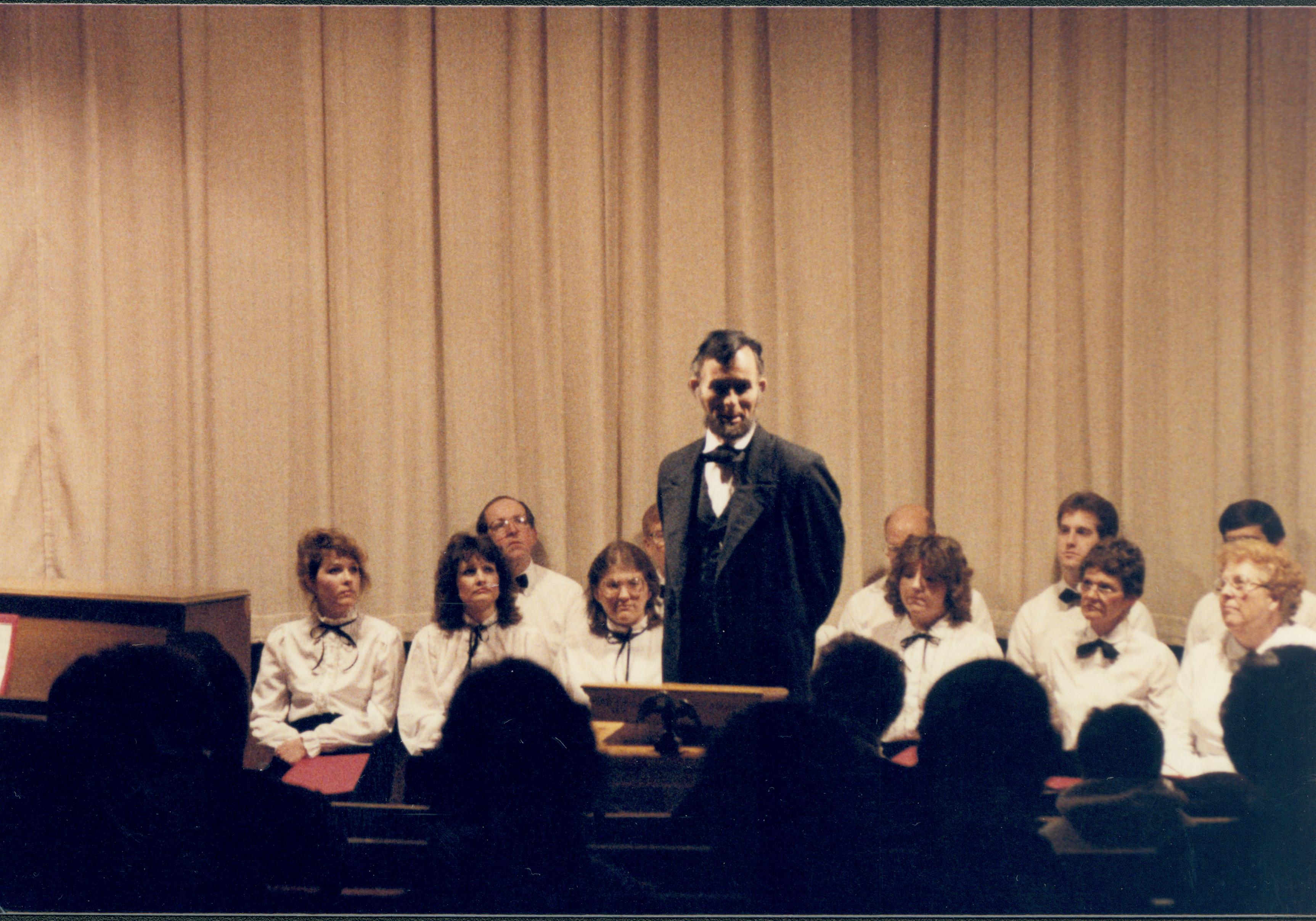 Lincoln impersonator speaking from podium, choral group seated behind. Lincoln Home NHS- Lincoln's Birthday 1988 birthday, Lincoln, Douglas