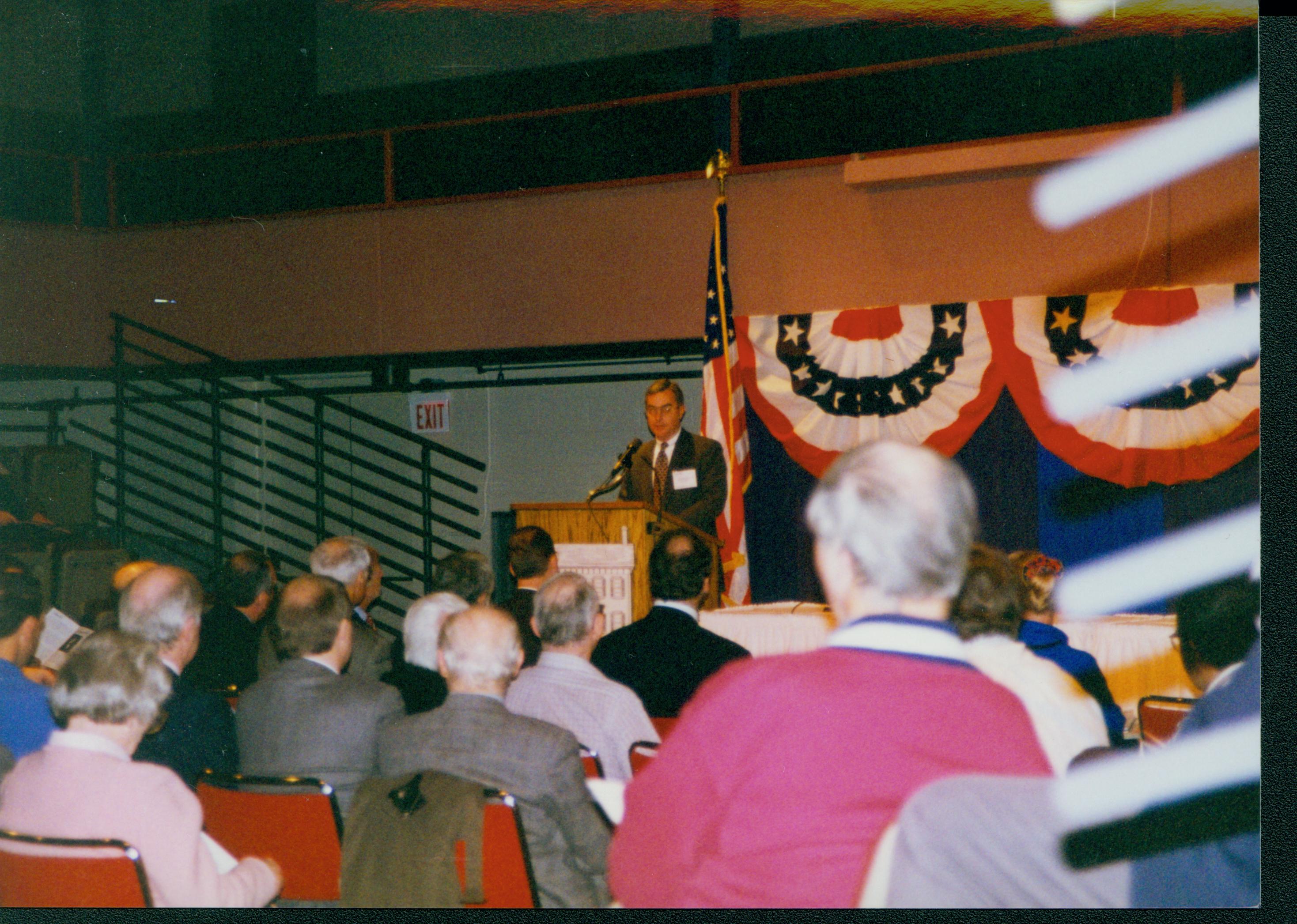 Man at posium with bunting hung behind. 1-1997 Colloq (color); 15 Colloquium, 1997