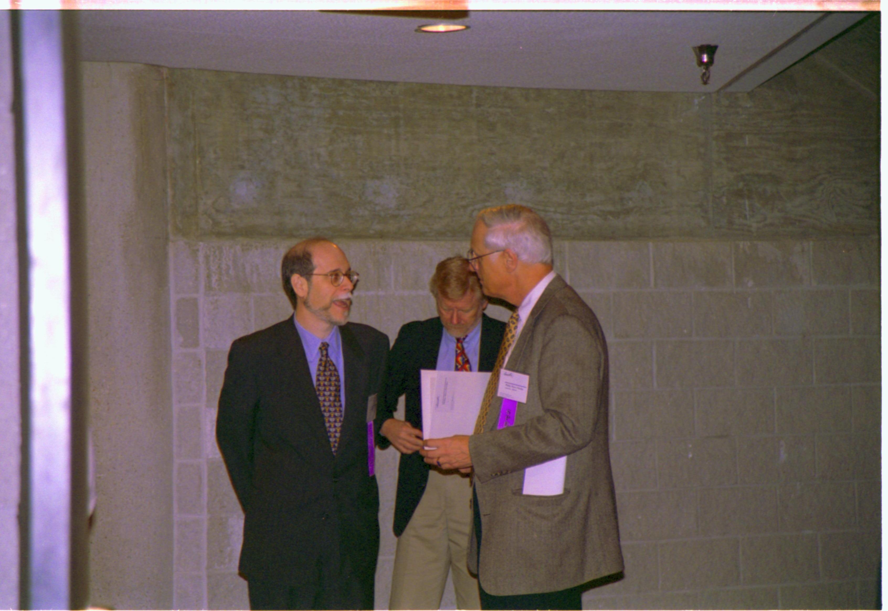 Three men standing in front of stone wall. 3-1997 Colloq (color); 5 Colloquium, 1997