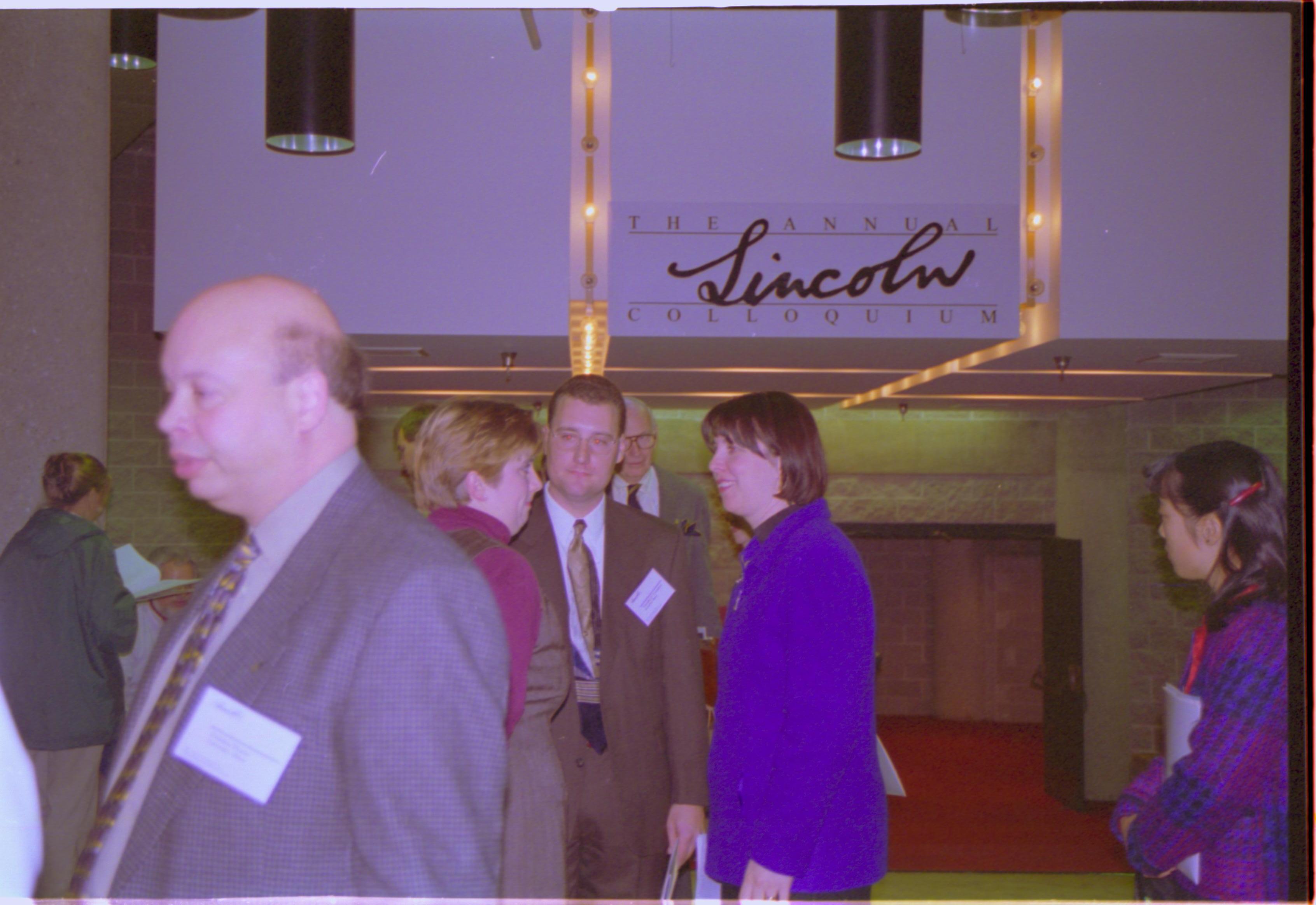 Three people talking under Colloquium sign. 3-1997 Colloq (color); 28 Colloquium, 1997