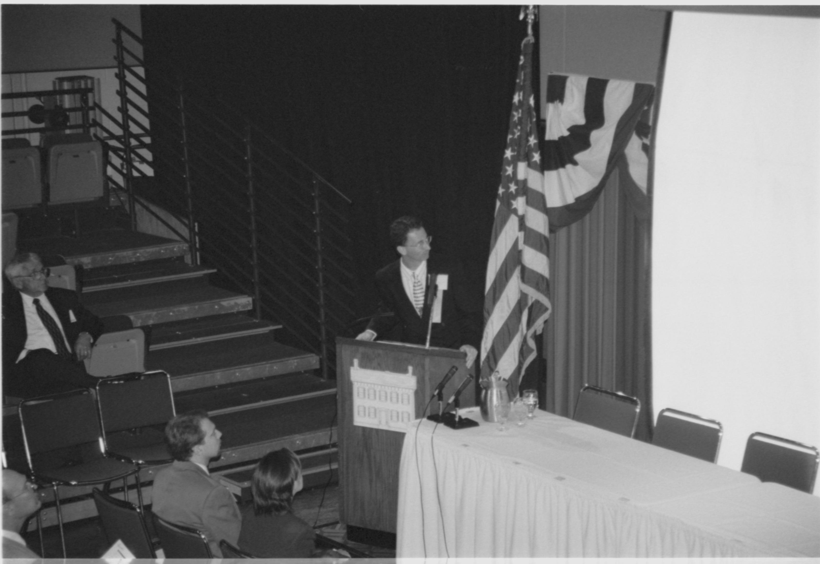 Speaker at podium looking at screen. 1999-16; 22 Colloquium, 1999