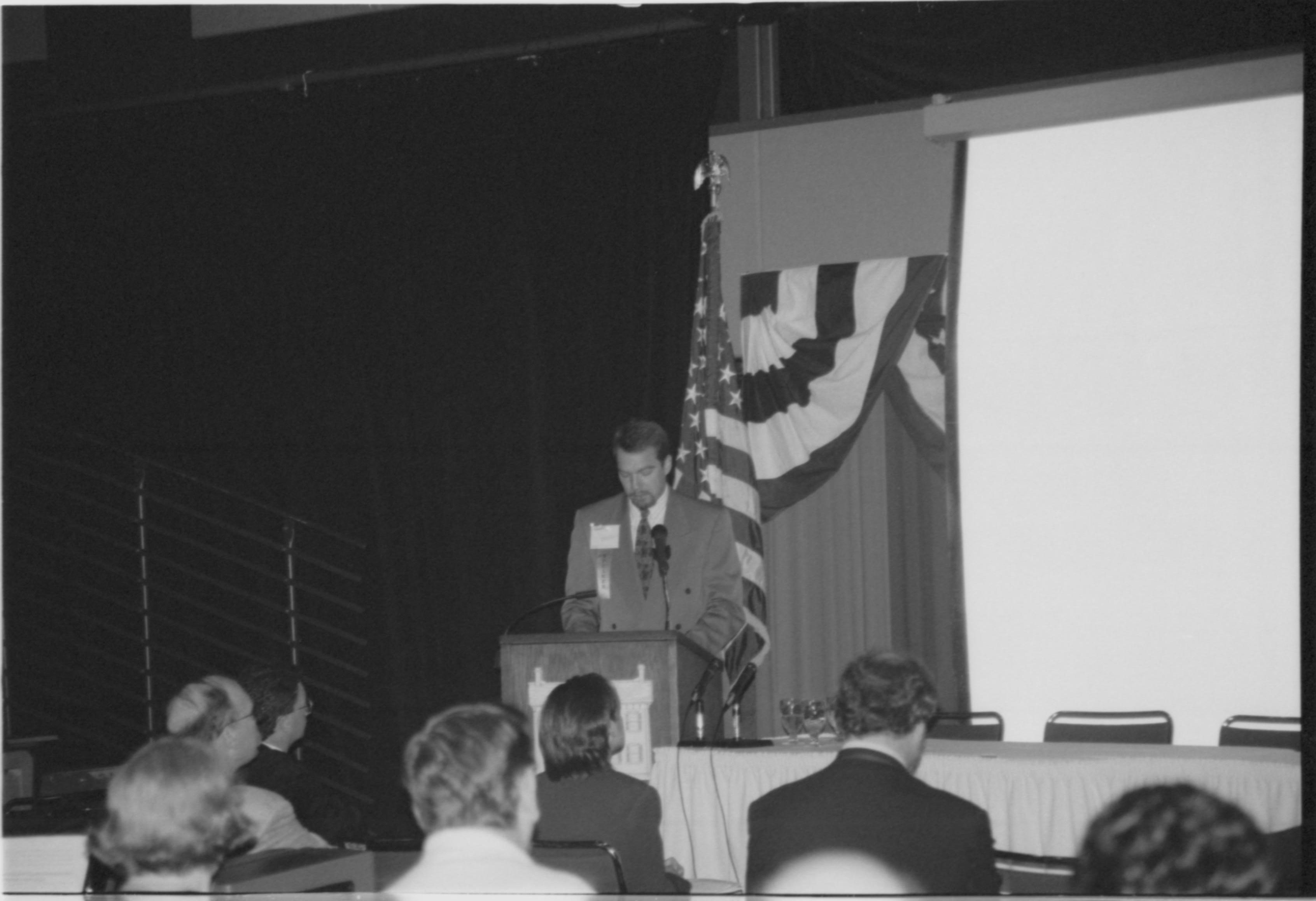 Man speaking at podium, looking down at notes.  1999-16; 25 Colloquium, 1999