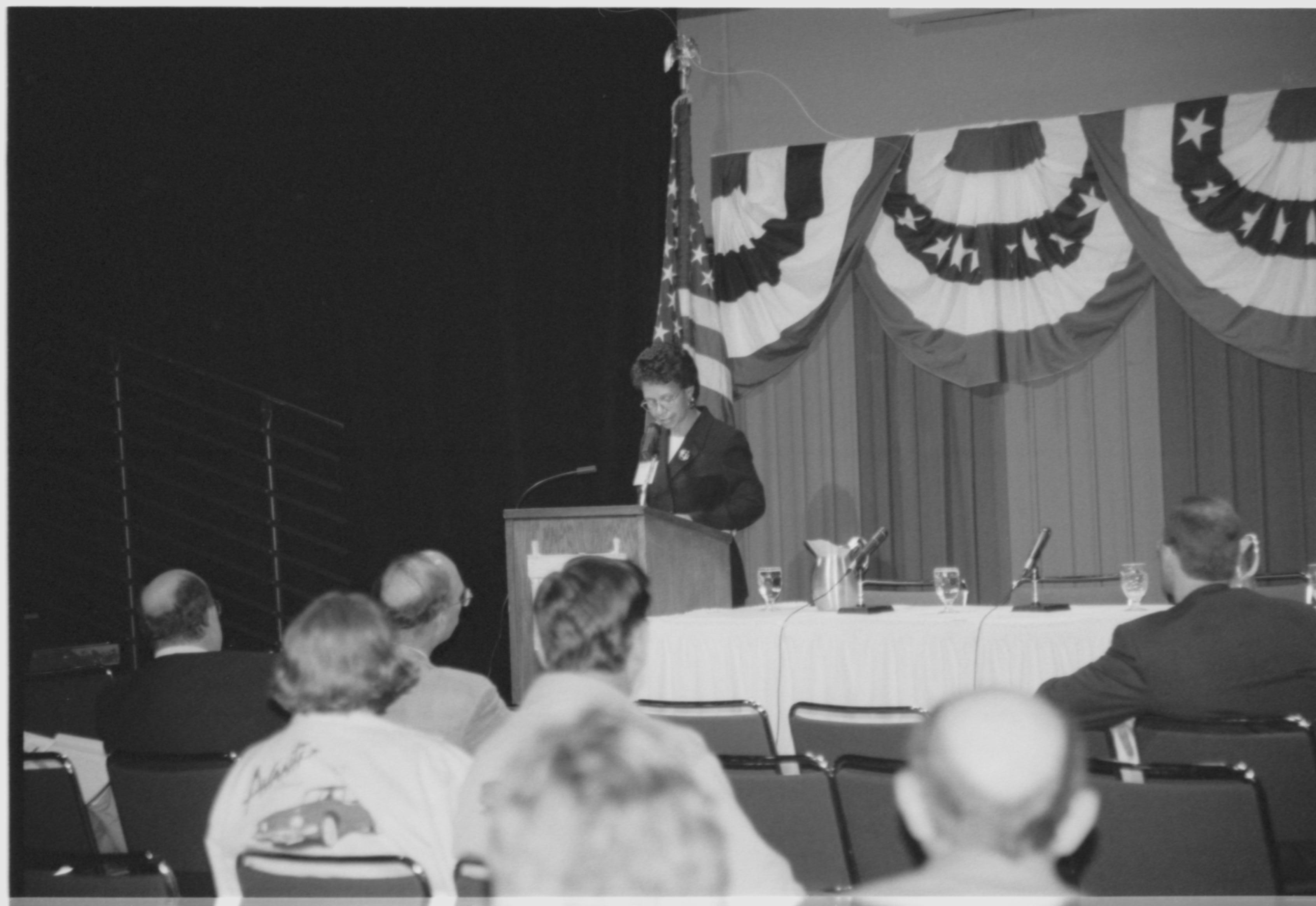Lady speaking at podium, looking at notes. 1999-16; 32 Colloquium, 1999