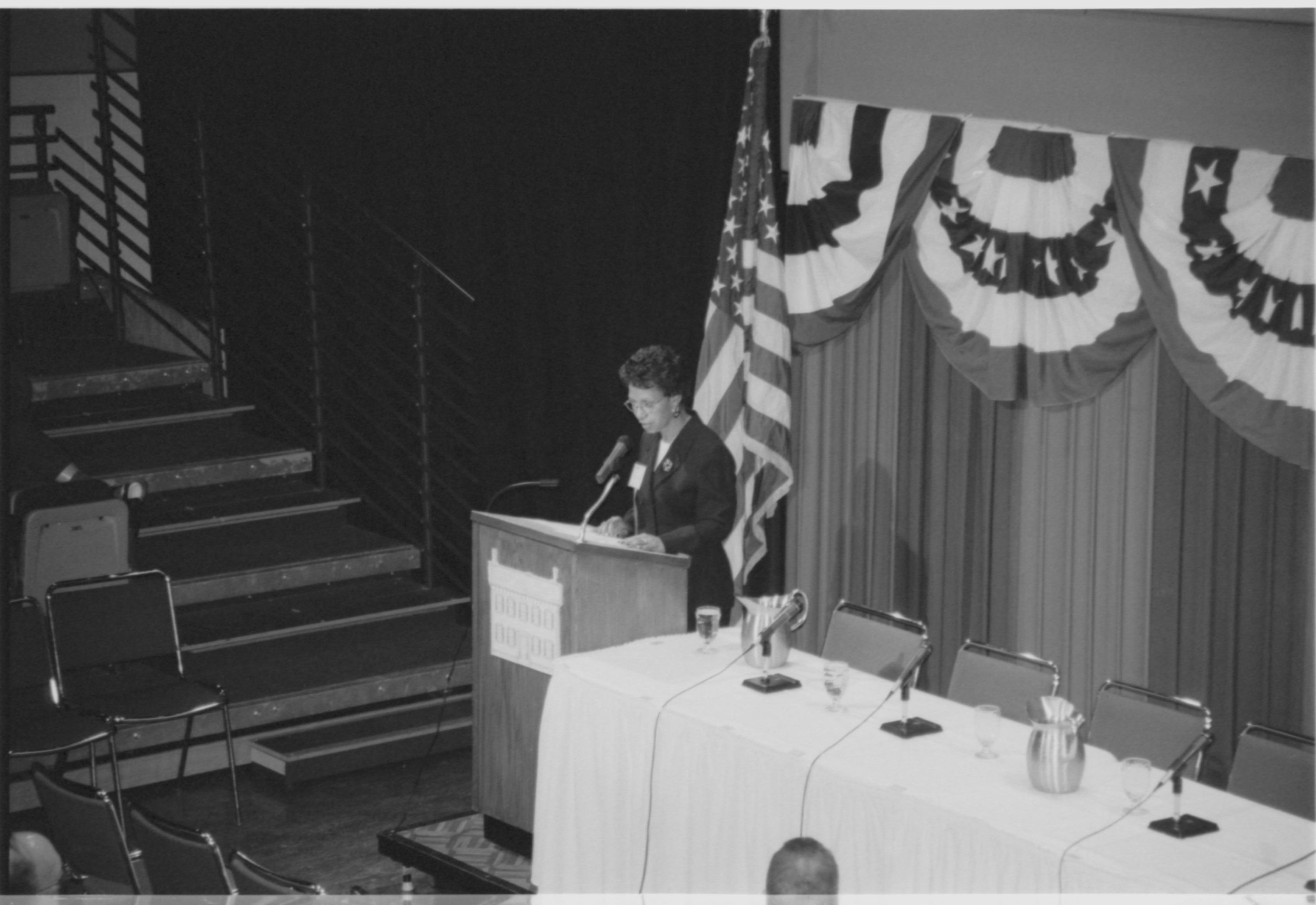 Lady speaking at podium, looking at notes. 1999-16; 33 Colloquium, 1999