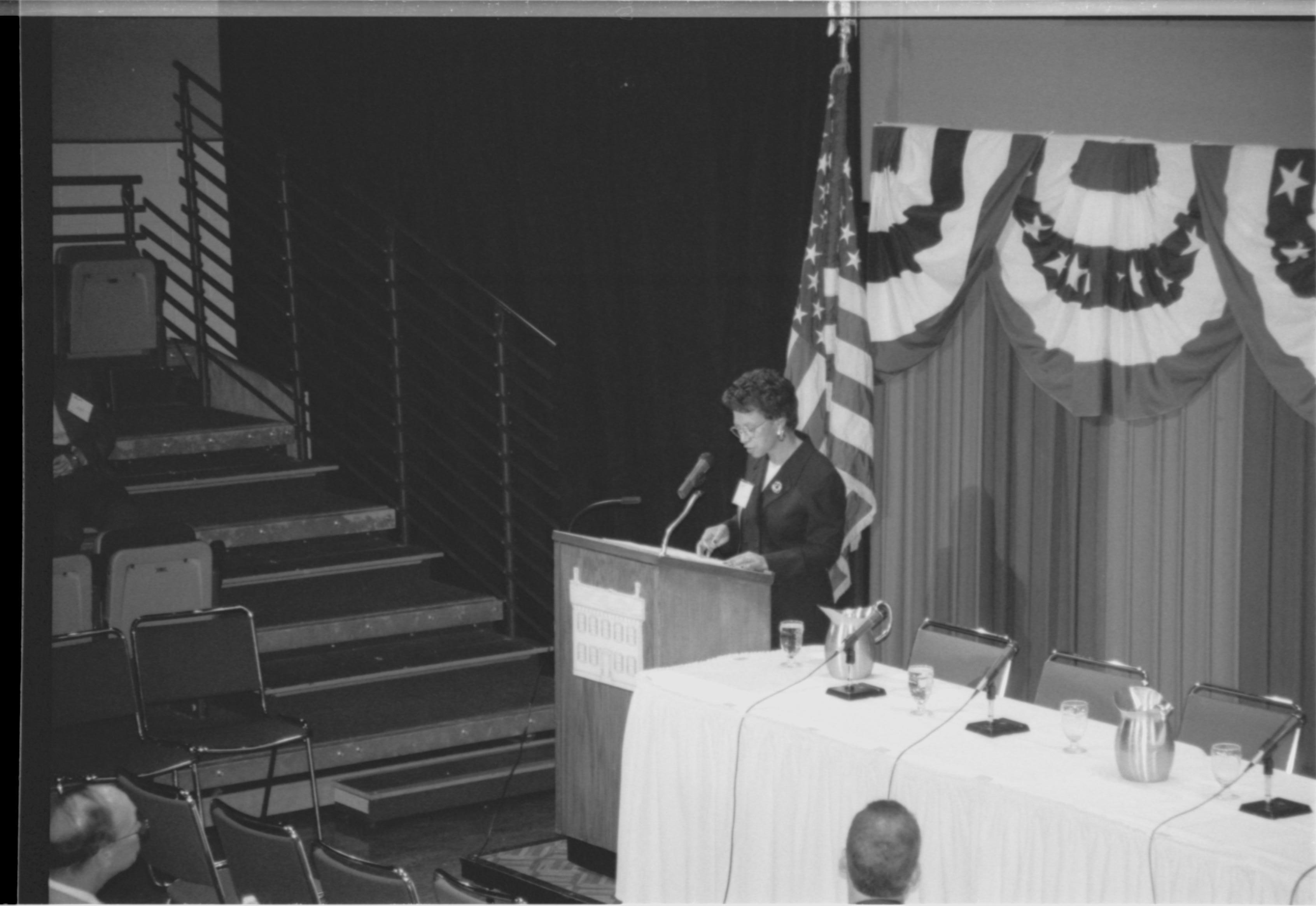 Lady speaking at podium, looking at notes. 1999-16; 36 Colloquium, 1999