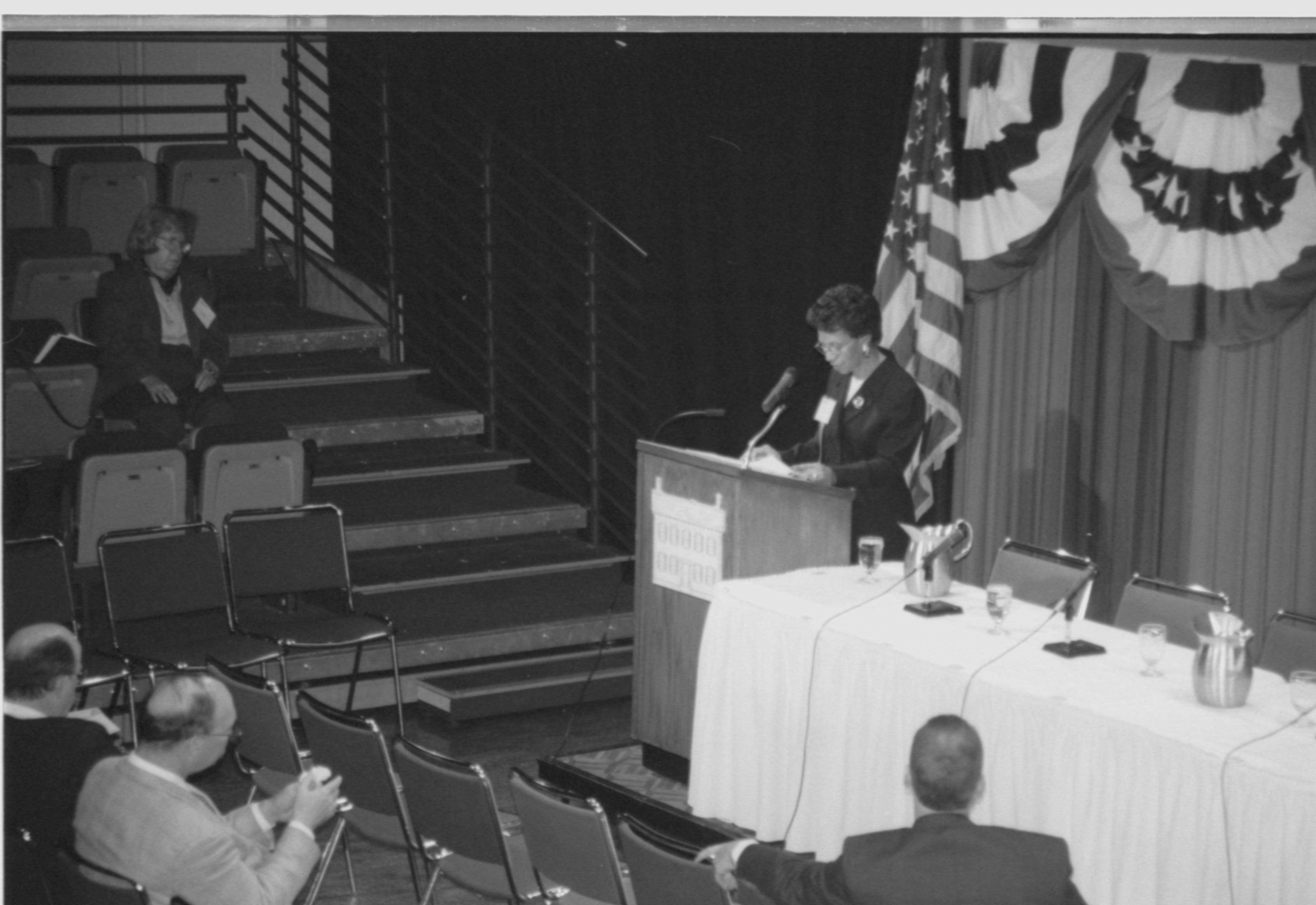 Lady speaking at podium, looking at notes. 1999-16; 37 Colloquium, 1999