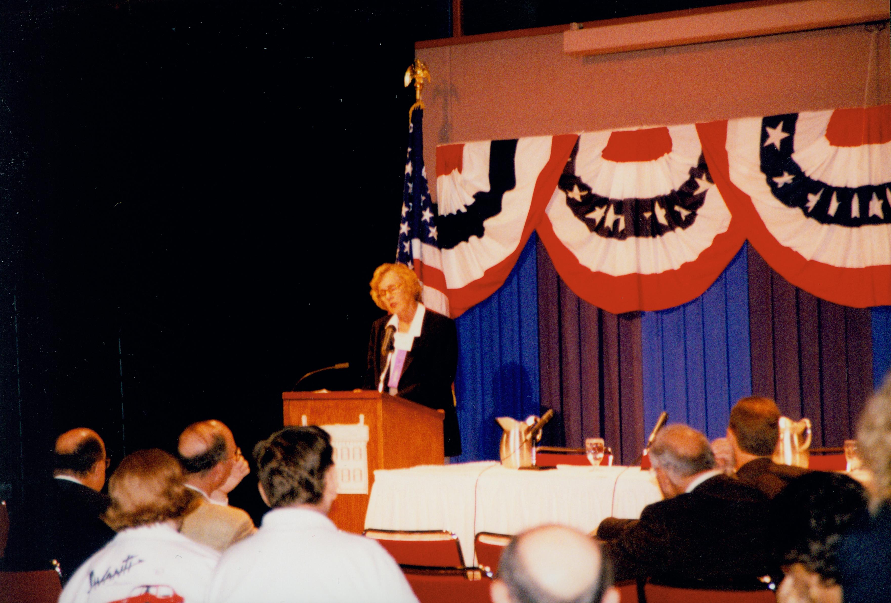 Lady (blond) speaking at podium (audience visable). 1999-12; 7 Colloquium, 1999
