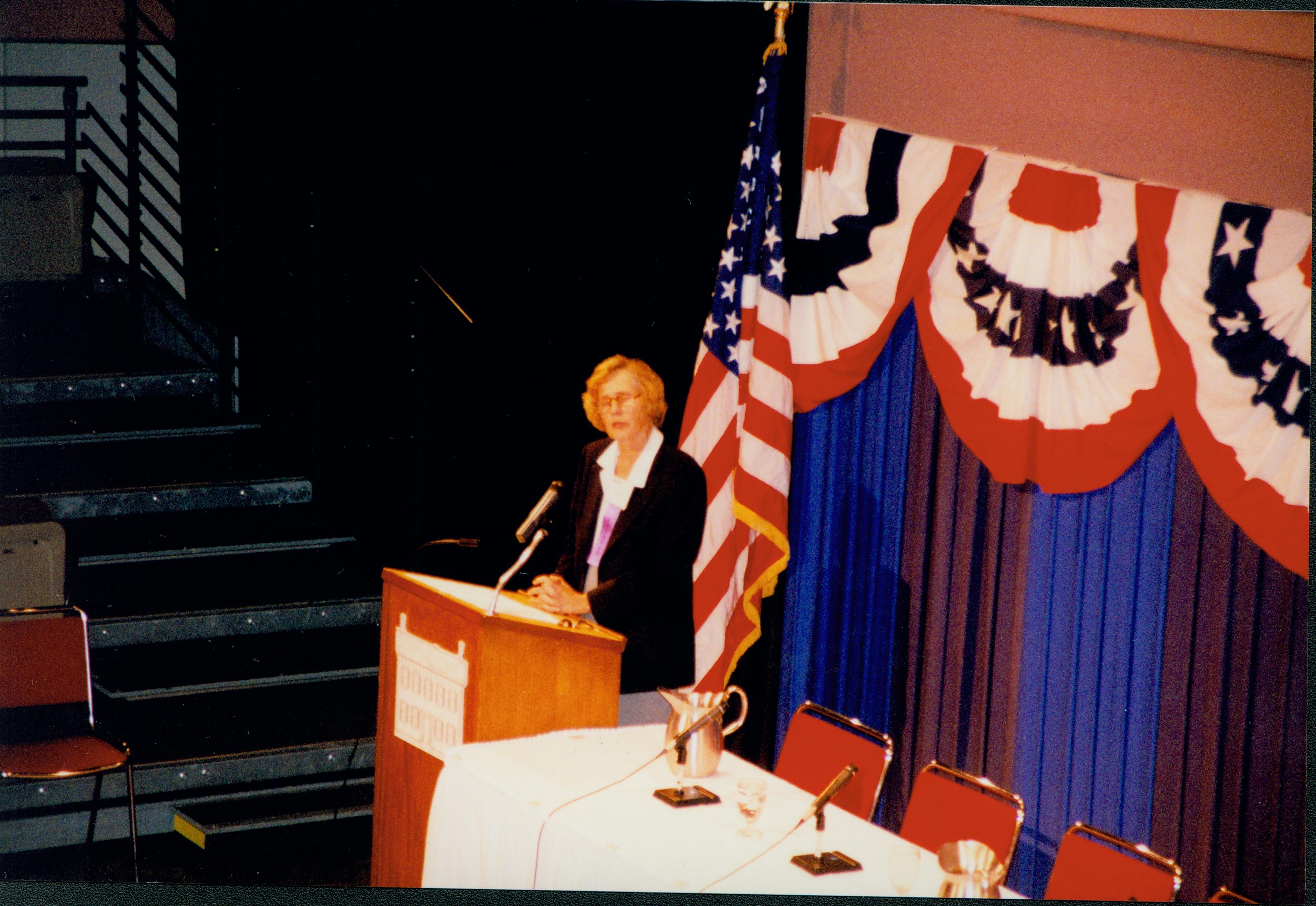 Lady (blond) speaking at podium. 1999-12; 8 Colloquium, 1999