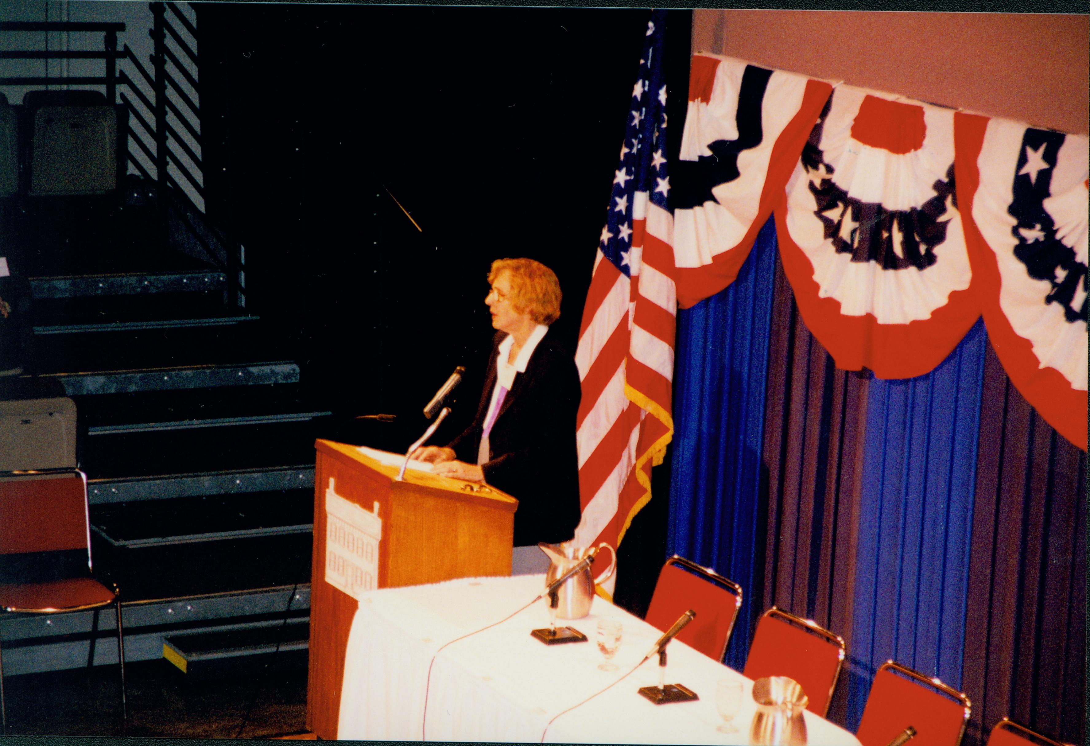 Lady (blond) speaking at podium (side view). 1999-12; 9 Colloquium, 1999