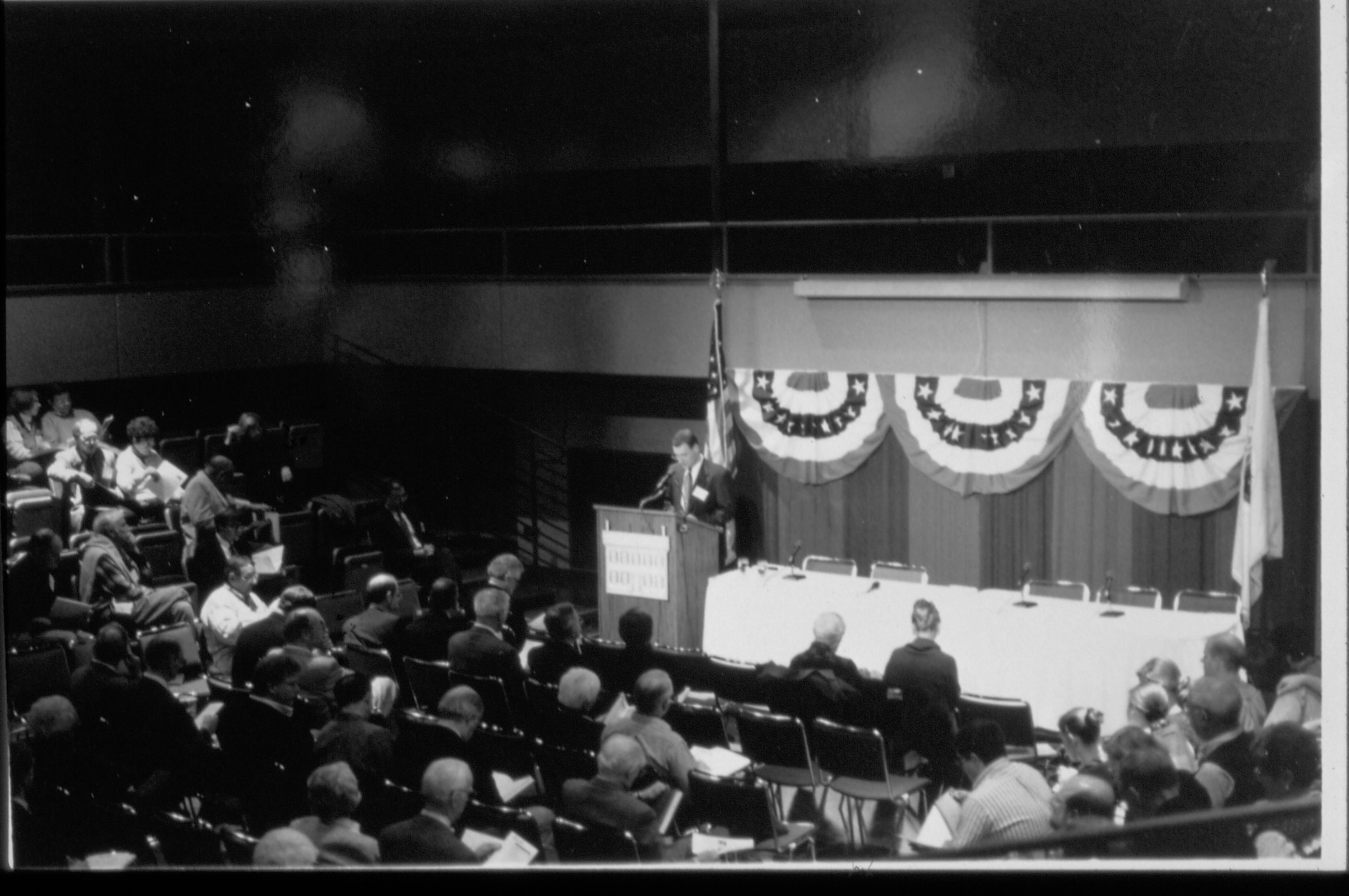Distant shot of speaker at podium and audience (b&w). Colloquium, 1999