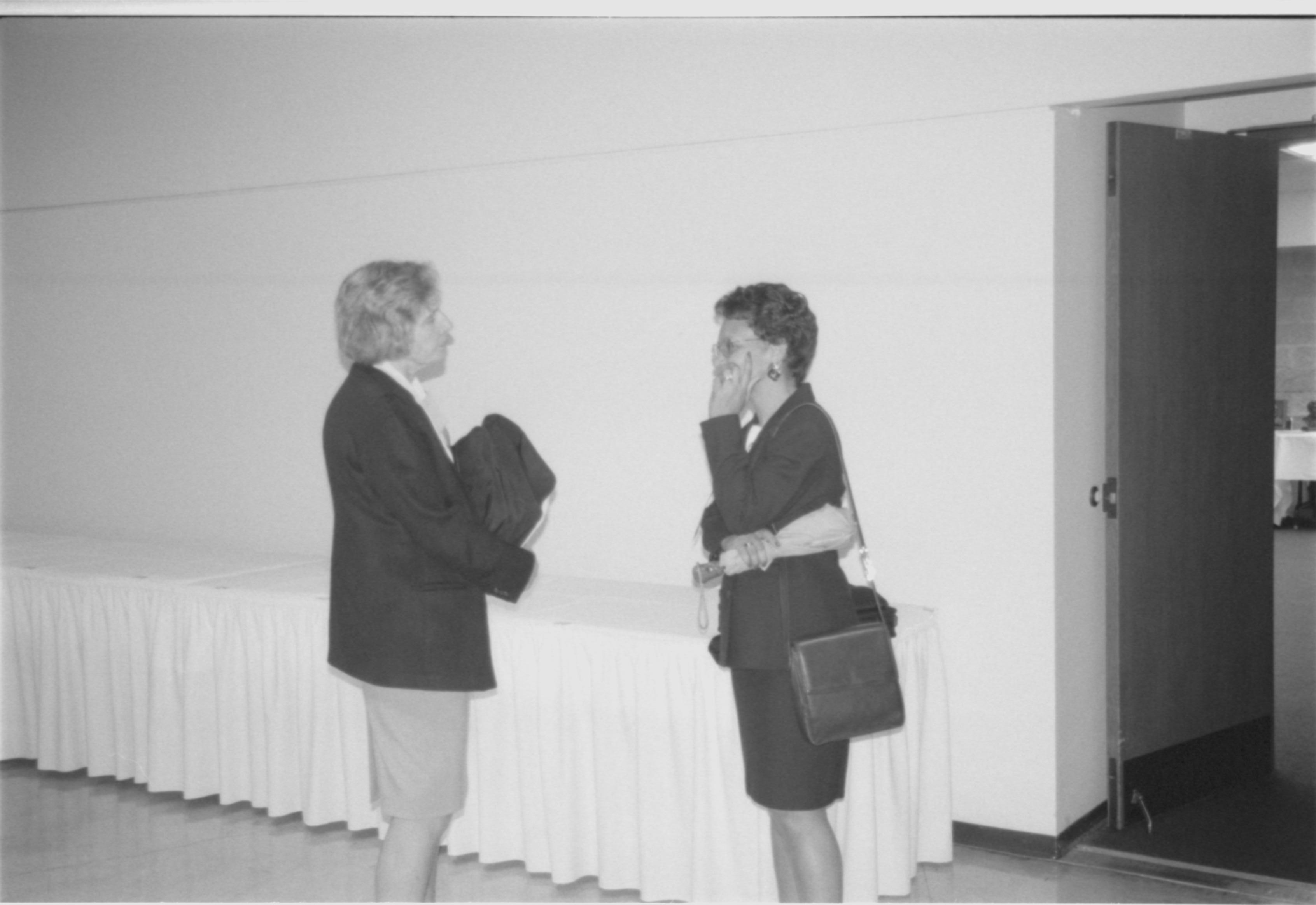 Two ladies standing, talking in front of curtain. 1999-16; 8 Colloquium, 1999