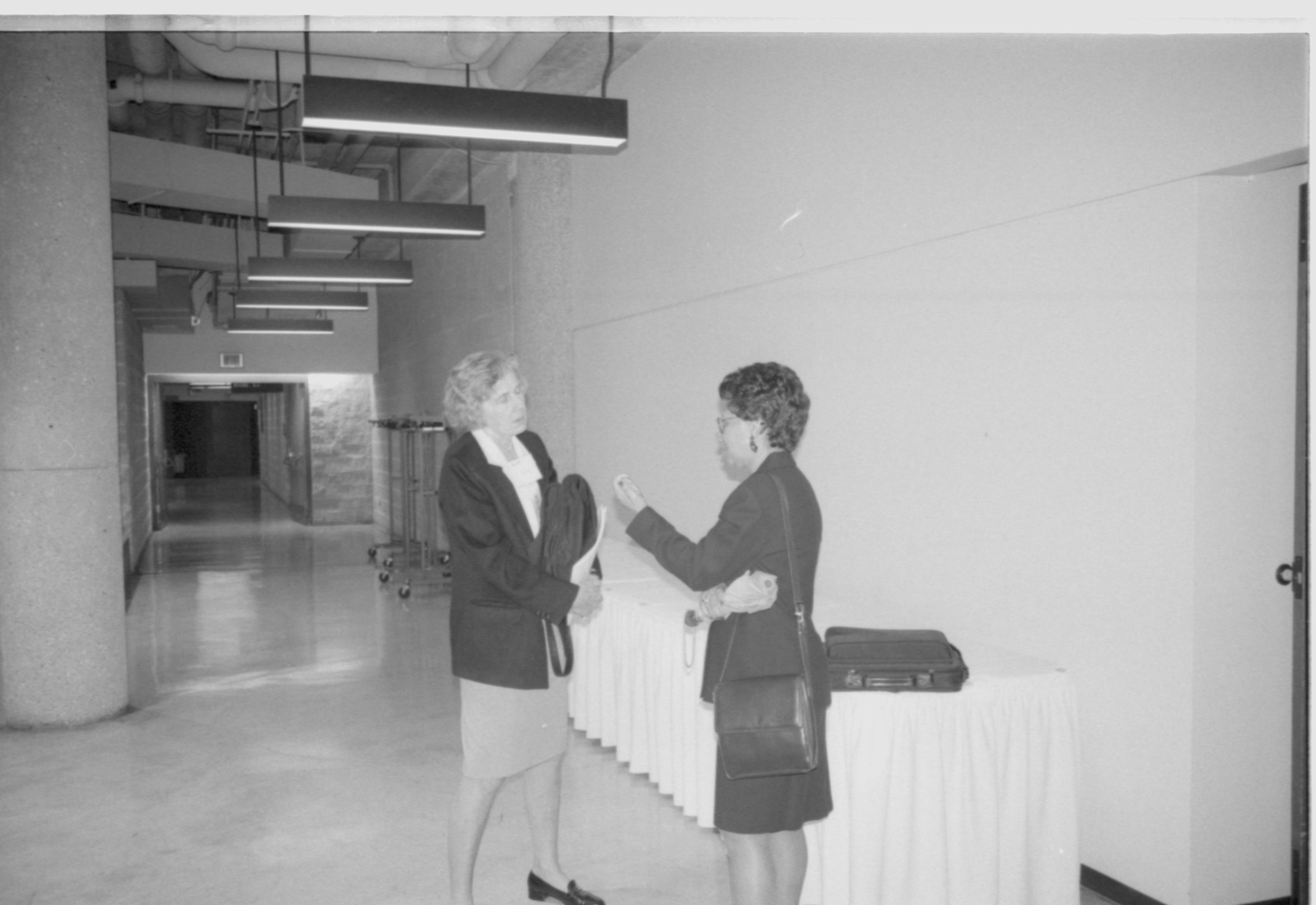 Two ladies standing, talking in front of curtain. 1999-16; 9 Colloquium, 1999