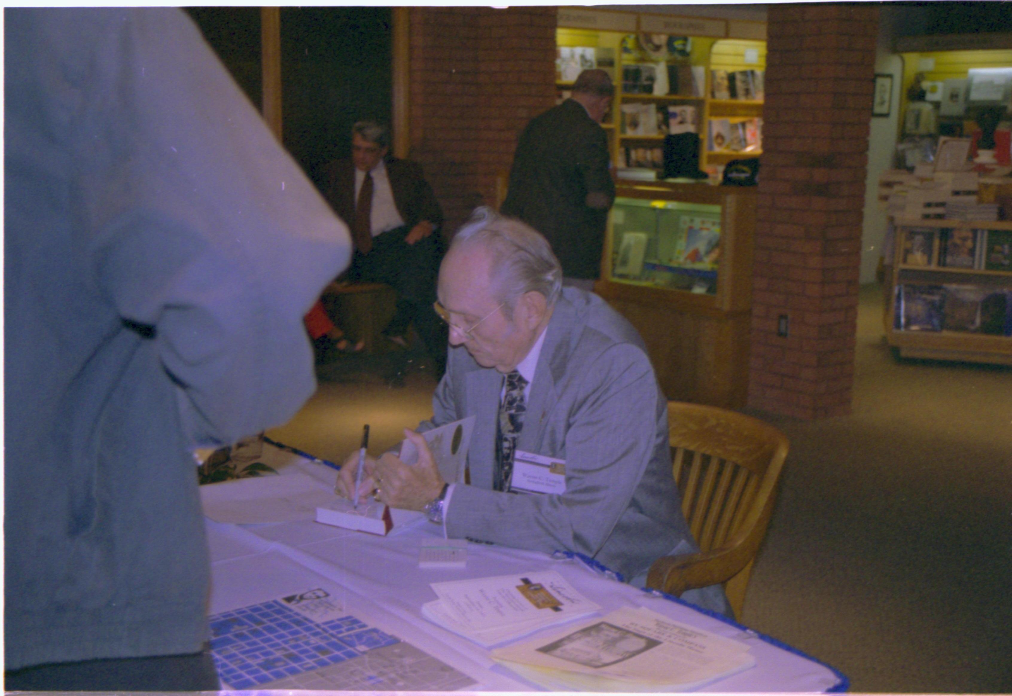 Man signing book at table. Colloquium