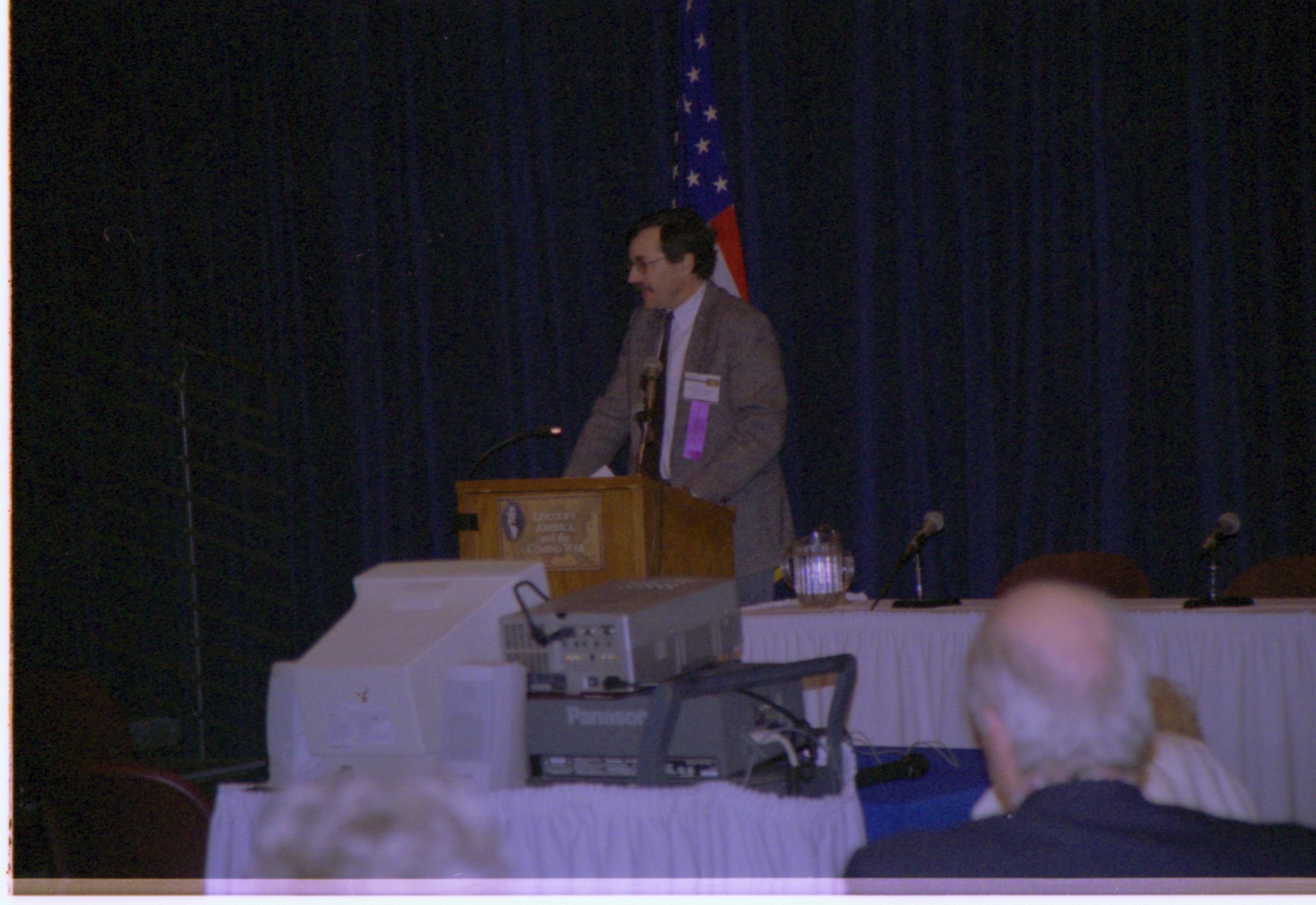 Speaker in brown suit at podium. Colloquium, 2001