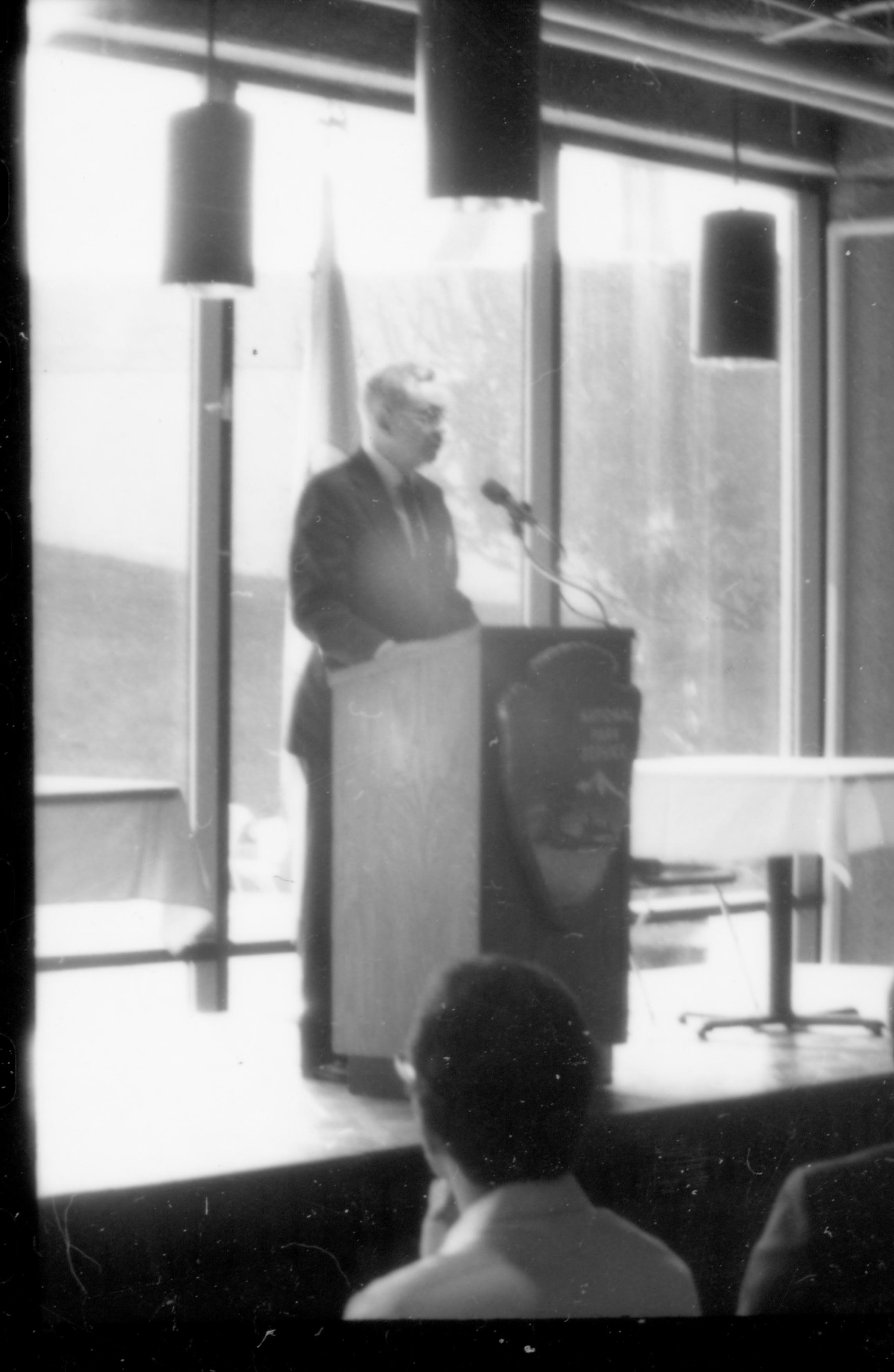 Man speaking at podium, glass windows behind. 1992 Lincoln Colloquium Lincoln, Colloquium