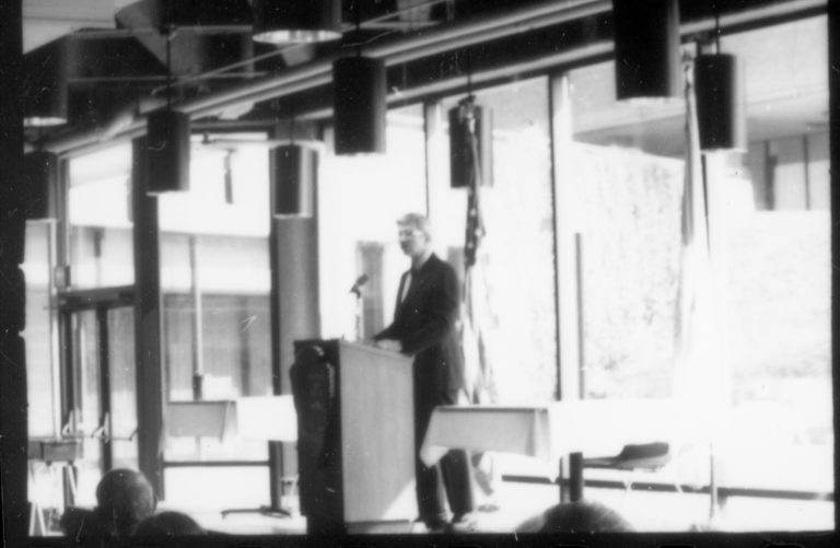 Man speaking at podium, glass windows behind. 1992 Lincoln Colloquium Lincoln, Colloquium