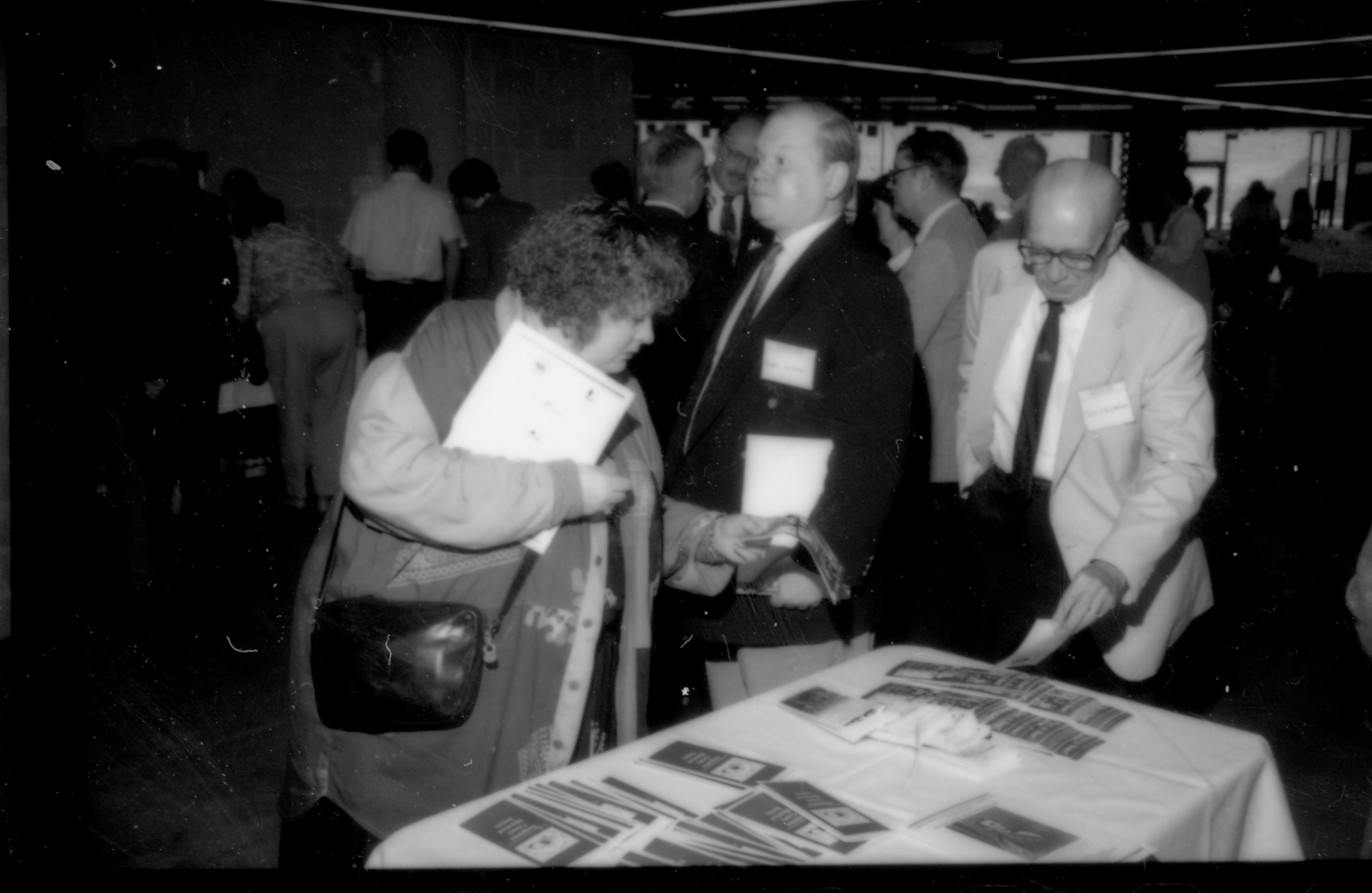 Lady and two men at literature table. 1992 Lincoln Colloquium; Outside #72 Lincoln, Colloquium