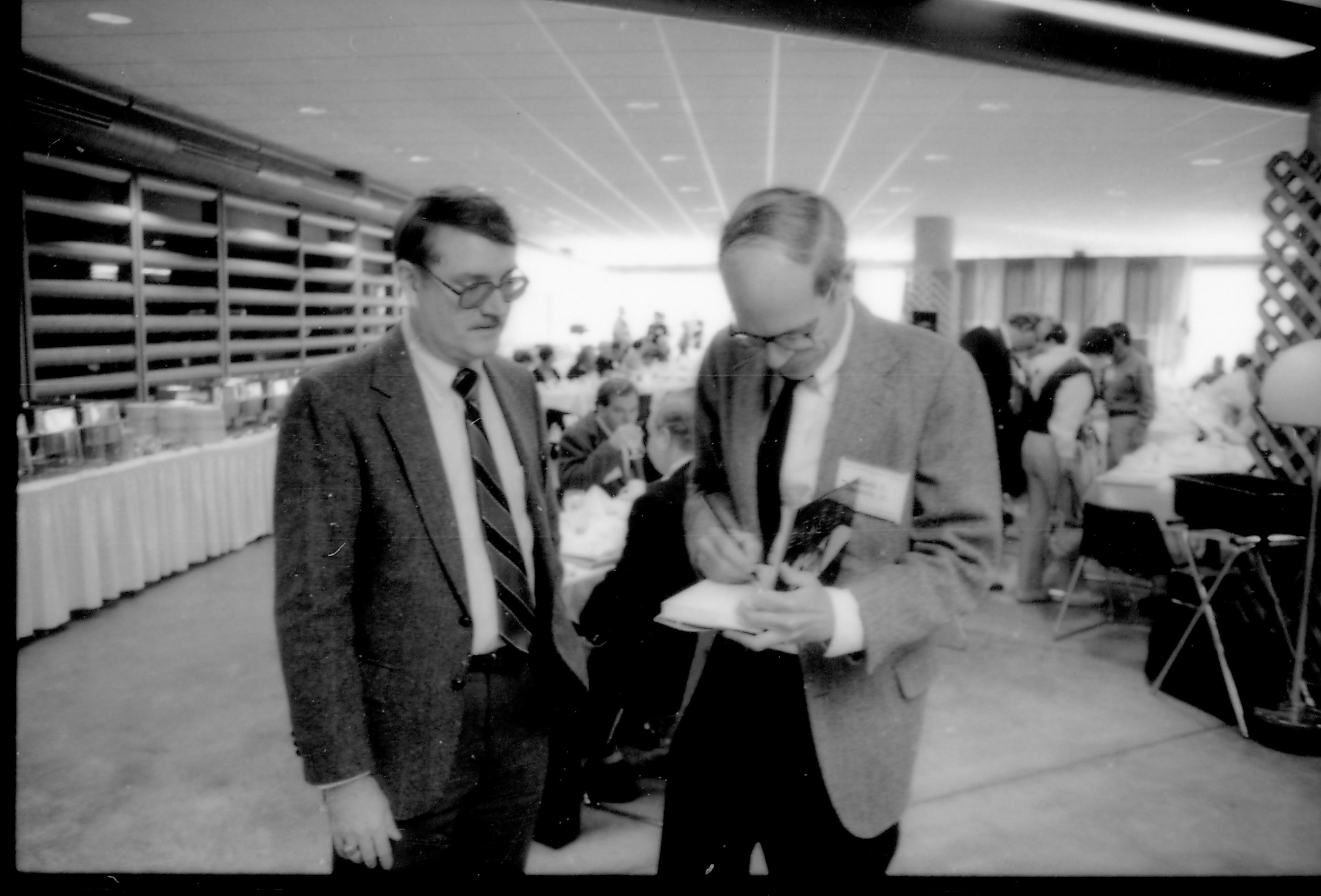 Two men standing, one signing book. 8th Annual Lincoln Colloquium; B Lincoln, Colloquium