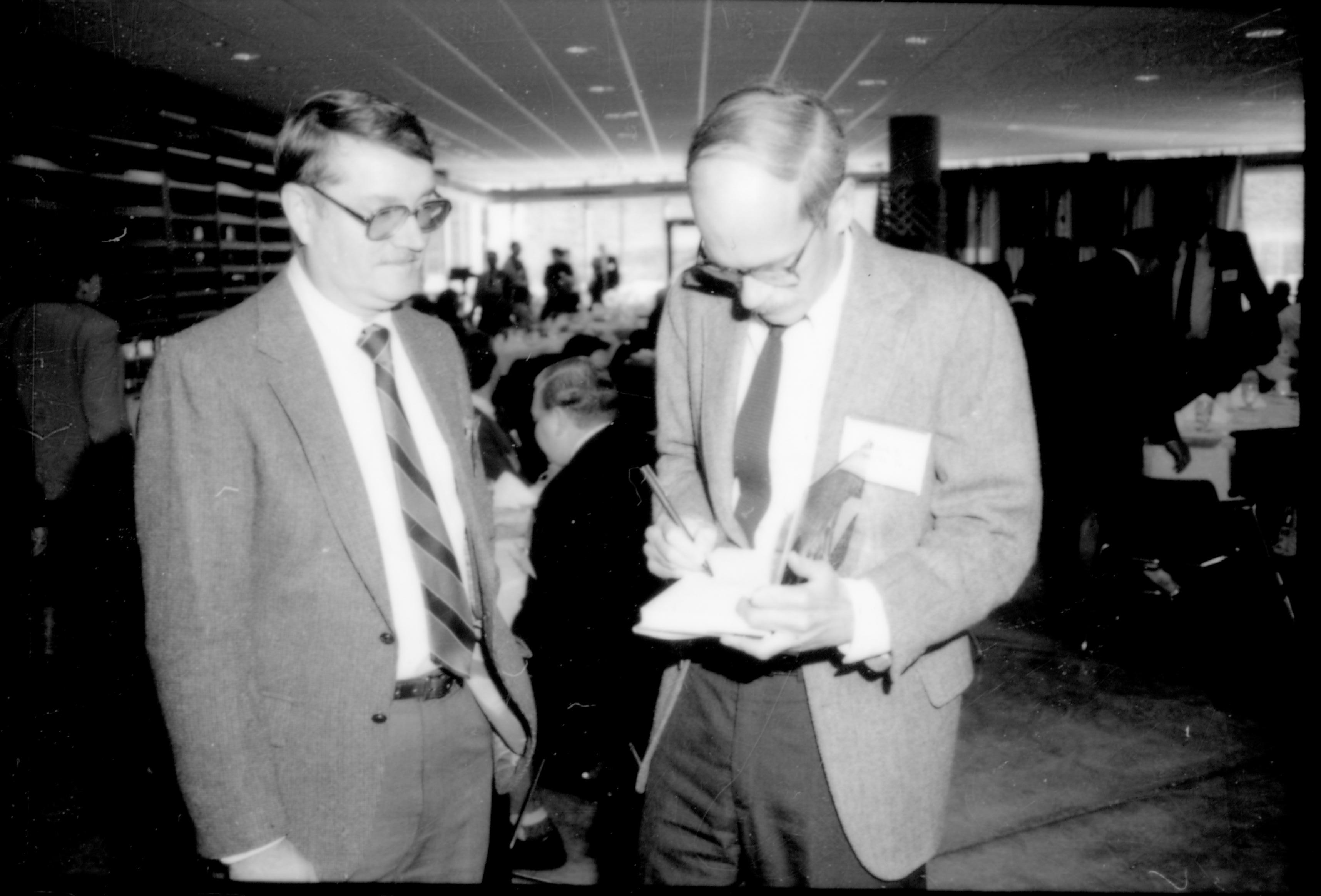 Two men standing, one signing book. 8th Annual Lincoln Colloquium; A Lincoln, Colloquium