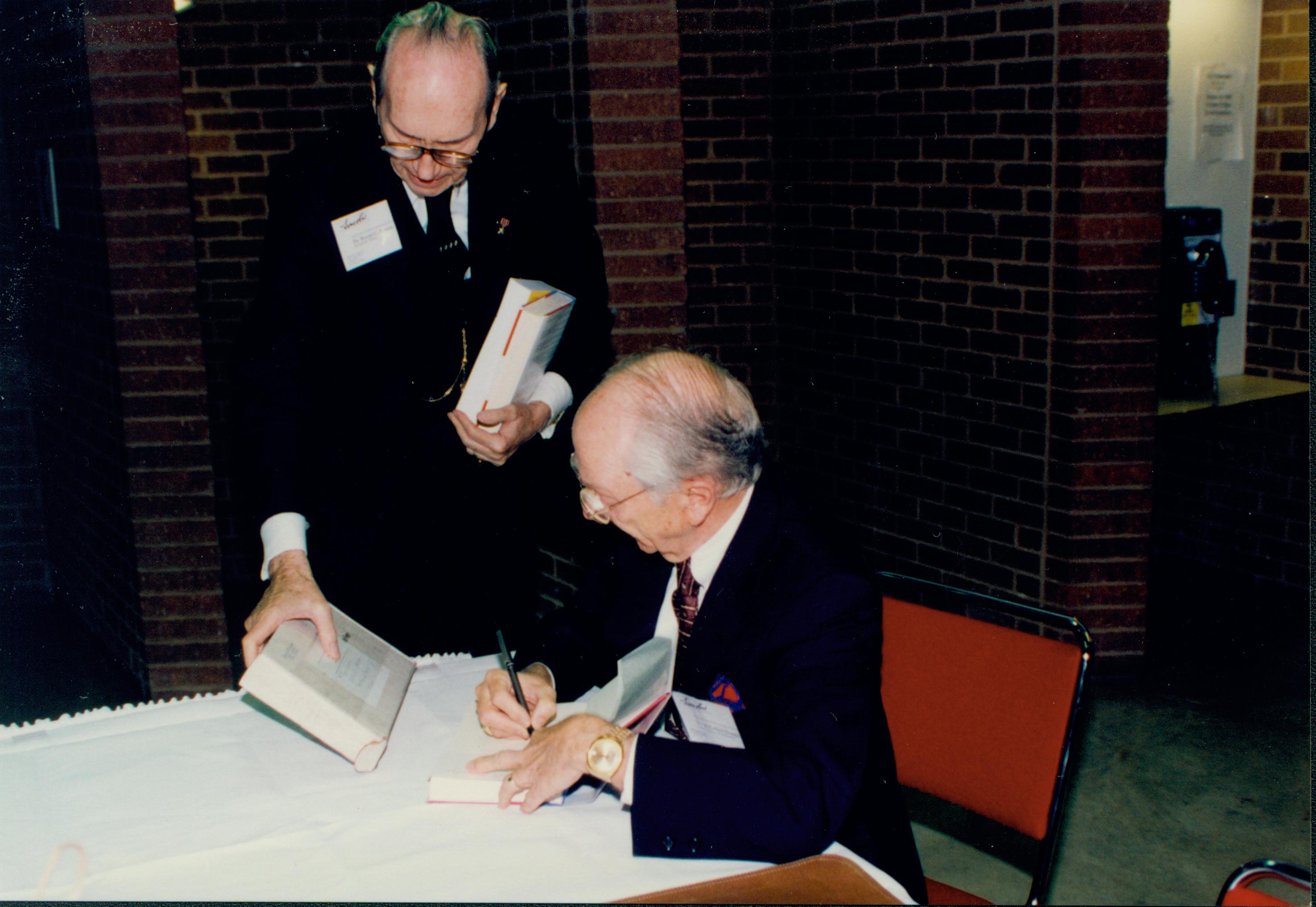 Man standing, one sitting signing a book. Lincoln Colloquium Lincoln, Colloquium