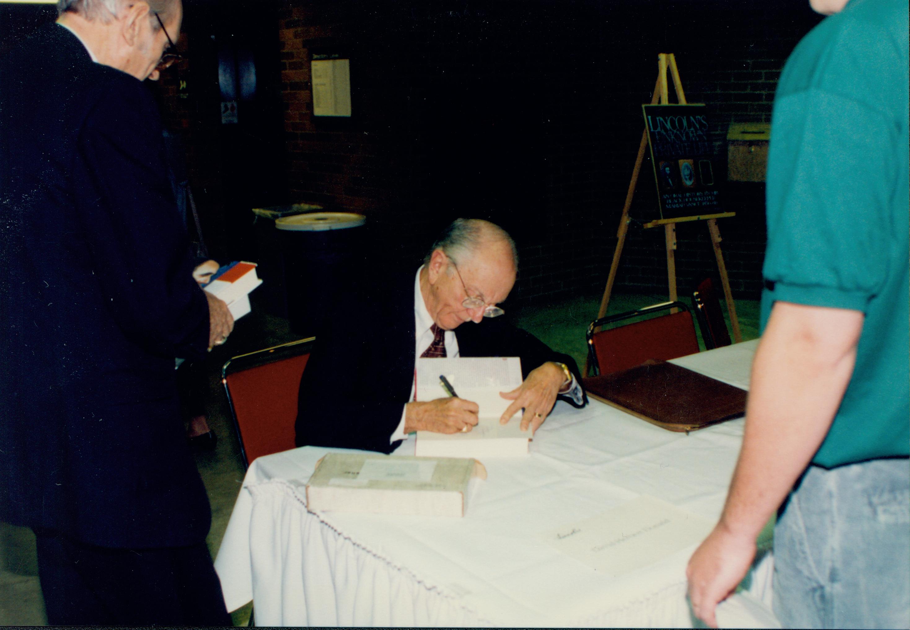 Man sitting signing book  Lincoln Colloquium Lincoln, Colloquium